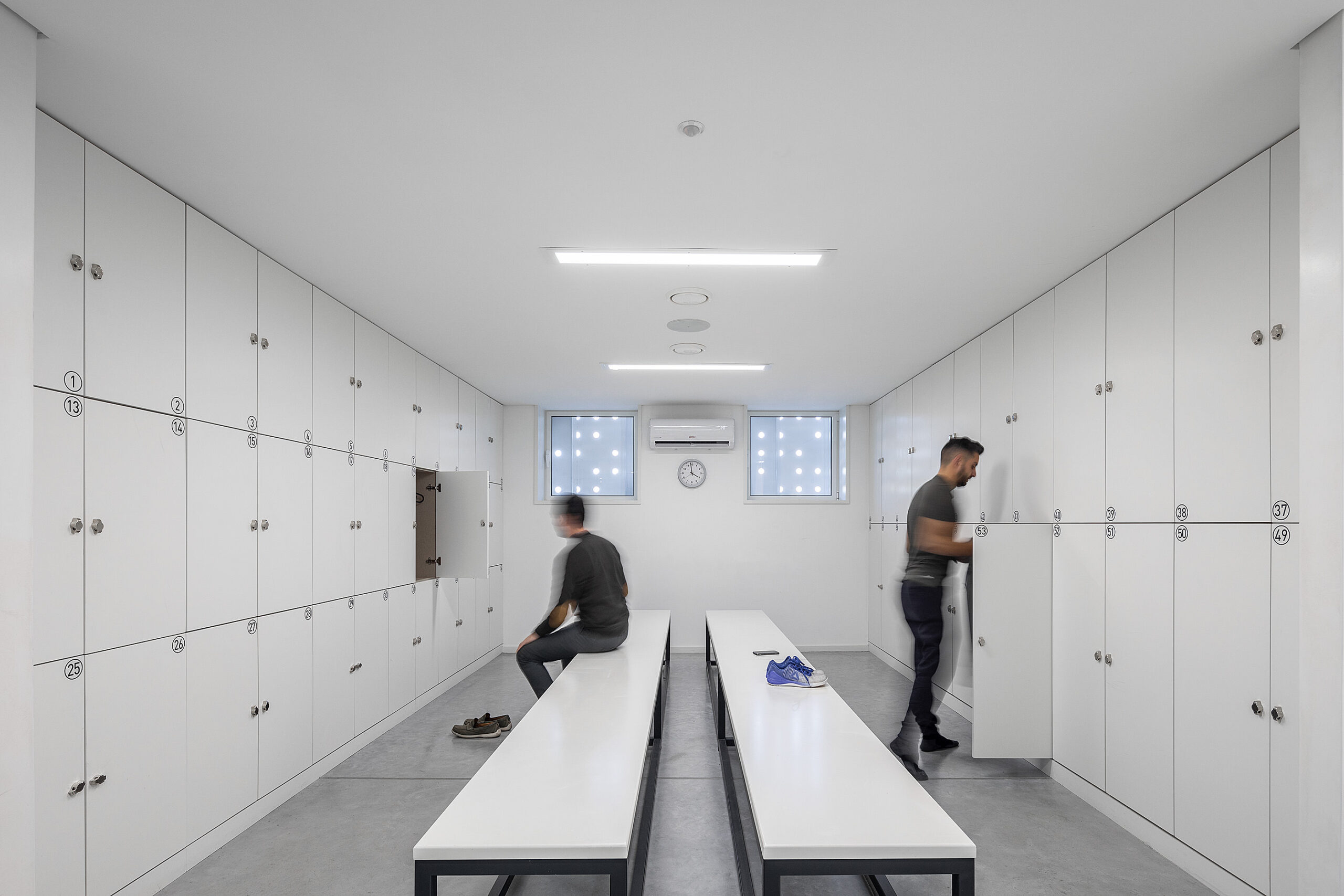 Vestiário com cacifos brancos e bancos. Iluminação linear e piso cinza. Design funcional. — Academia20 arquitetura StudioWorkers em Espinho