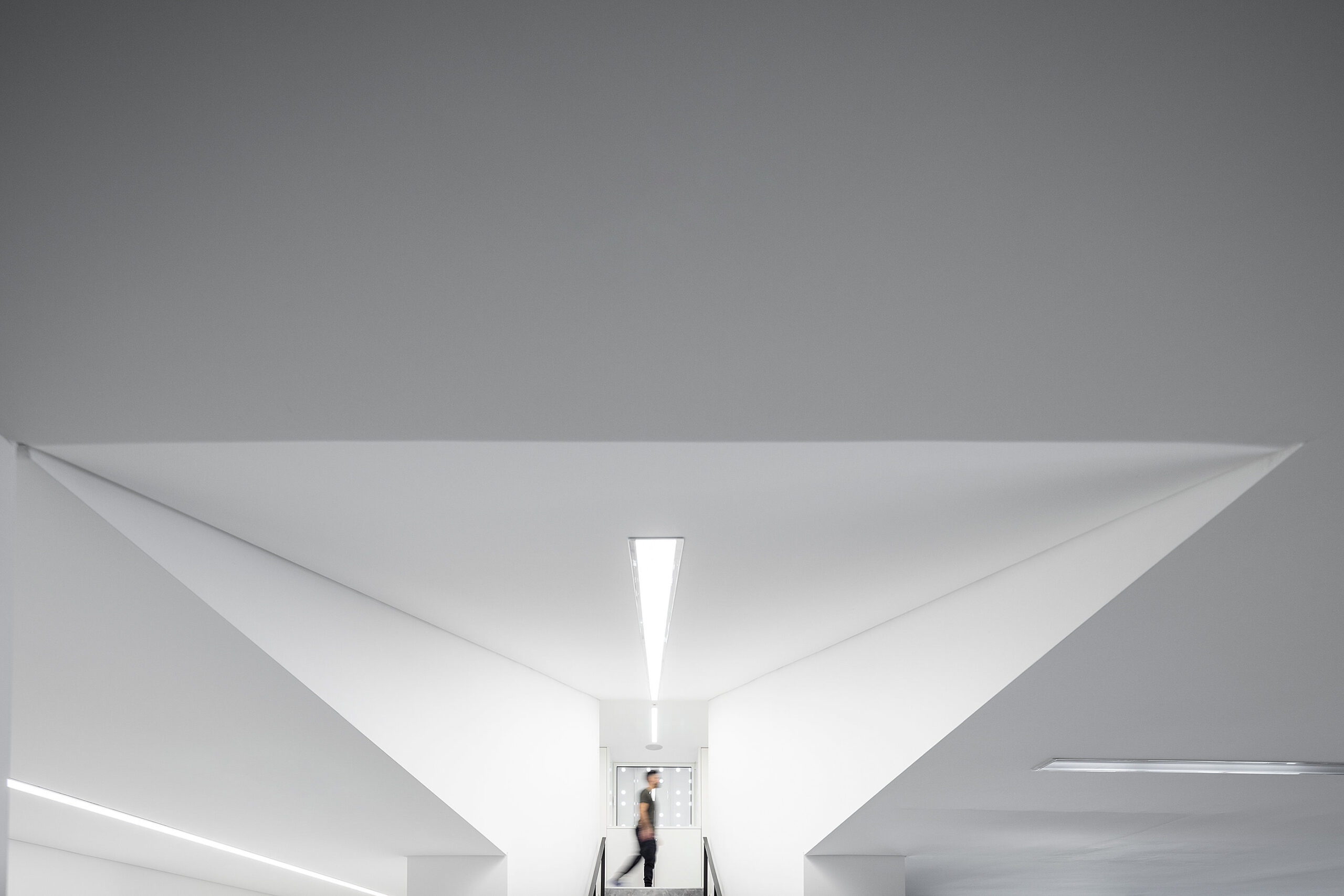 Detalhe do teto com iluminação linear e pessoa a subir escadas. Design minimalista e moderno. — Academia20 arquitetura StudioWorkers em Espinho