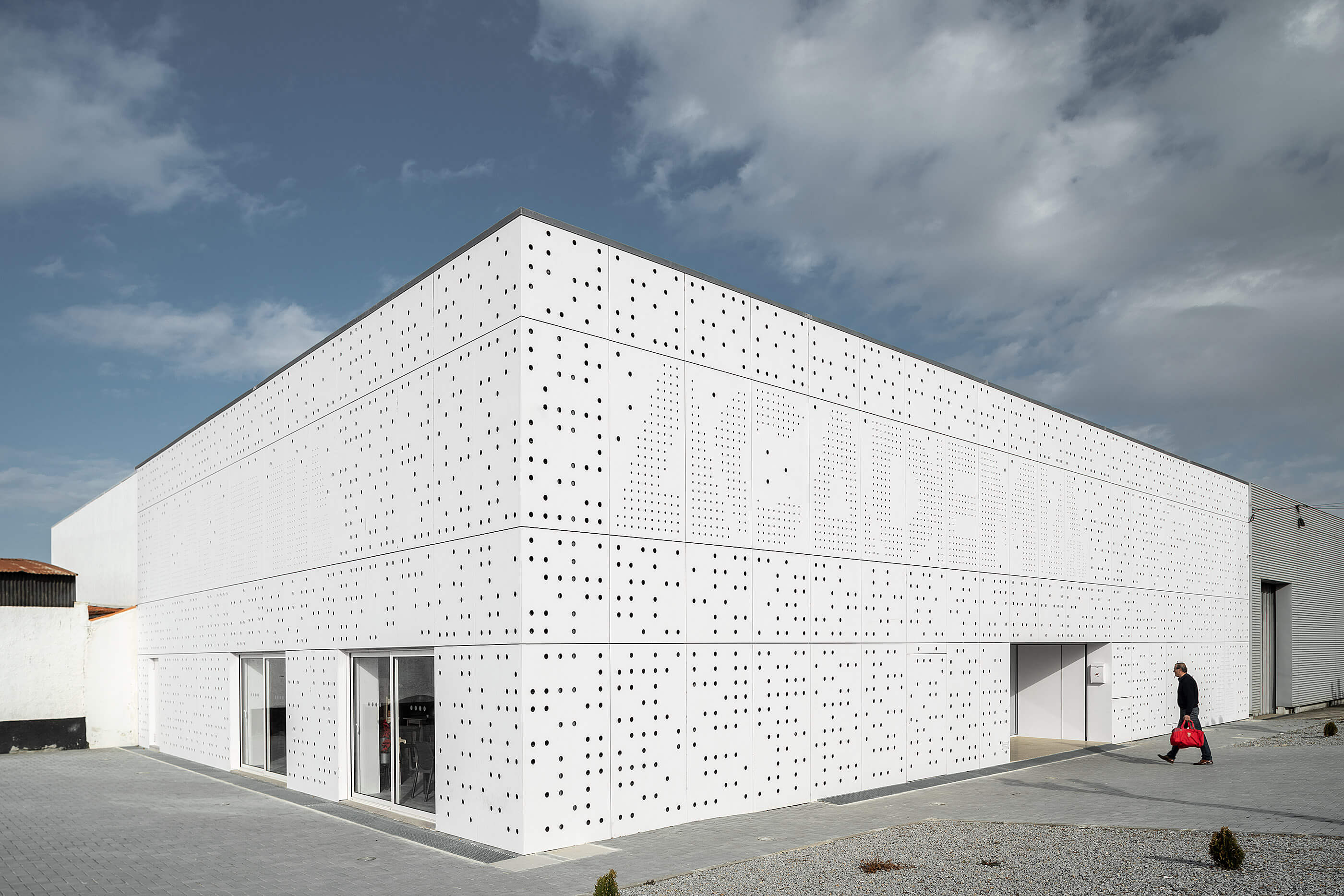 Edifício branco com fachada perfurada. Entrada envidraçada e paisagem urbana. — Academia20 arquitetura StudioWorkers em Espinho