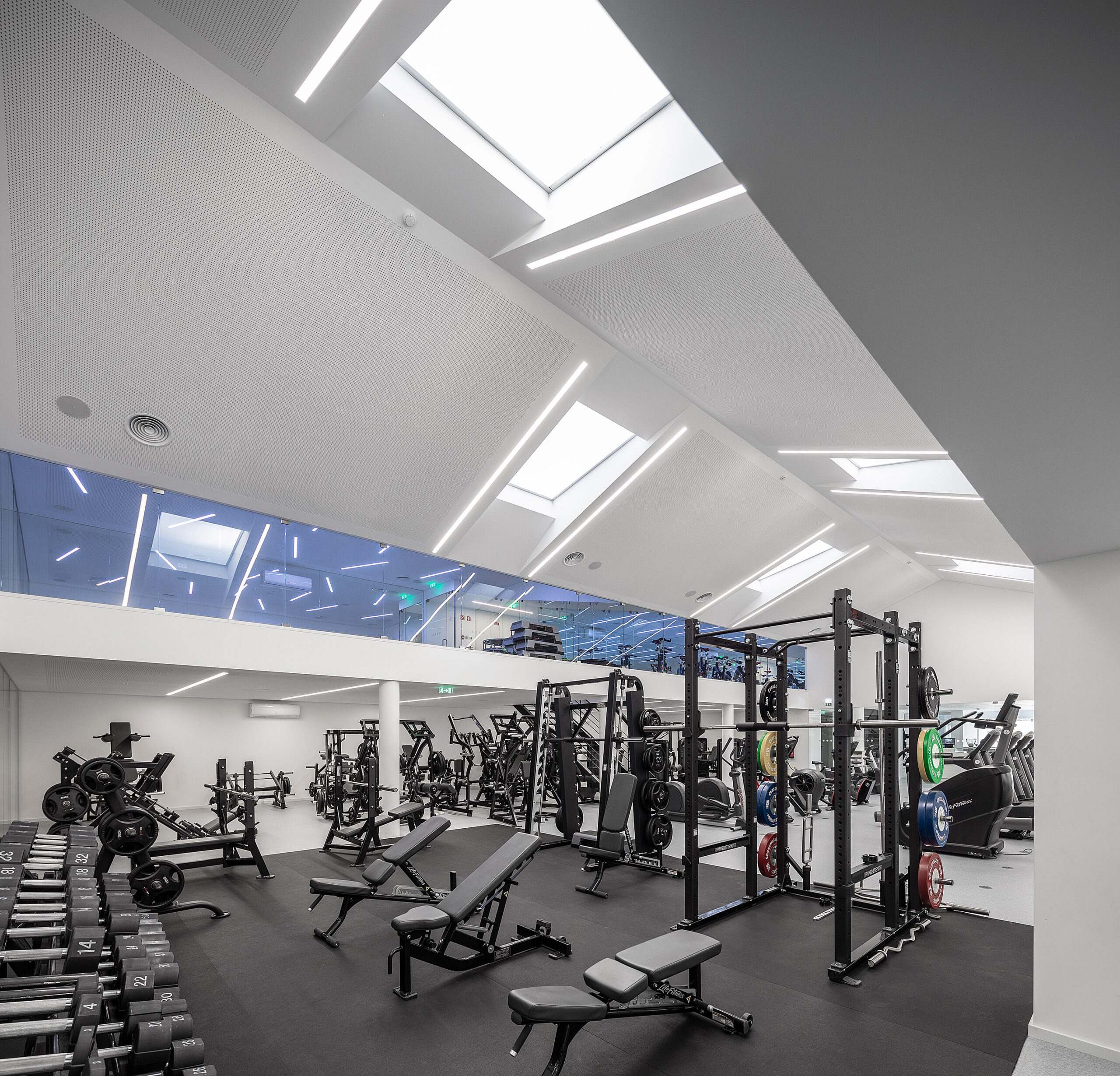 Ginásio amplo com equipamentos pretos, piso em borracha e claraboias. Design moderno e clean. — Academia20 arquitetura StudioWorkers em Espinho