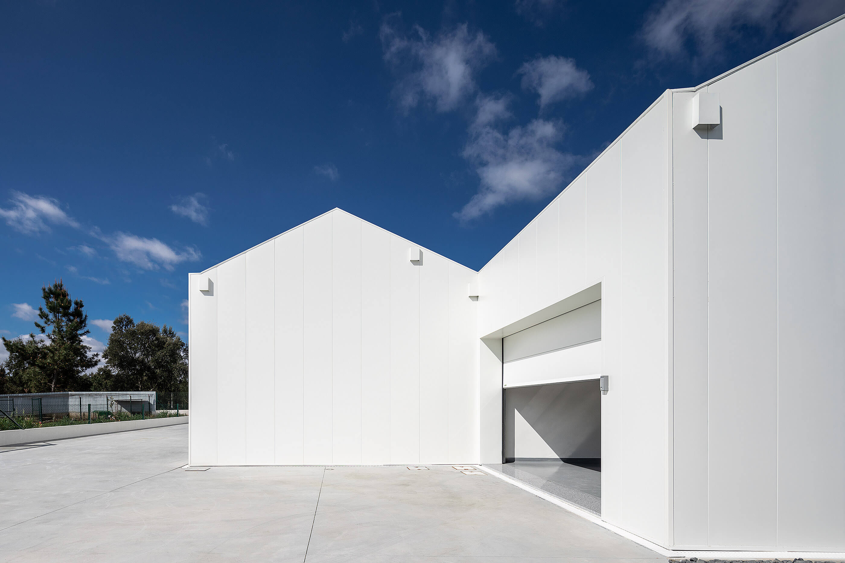 Vista lateral da adega branca, com porta de acesso e pavimento exterior em betão. — Adega do Castanheirinho arquitetura João Albano Arquitecto em Águeda