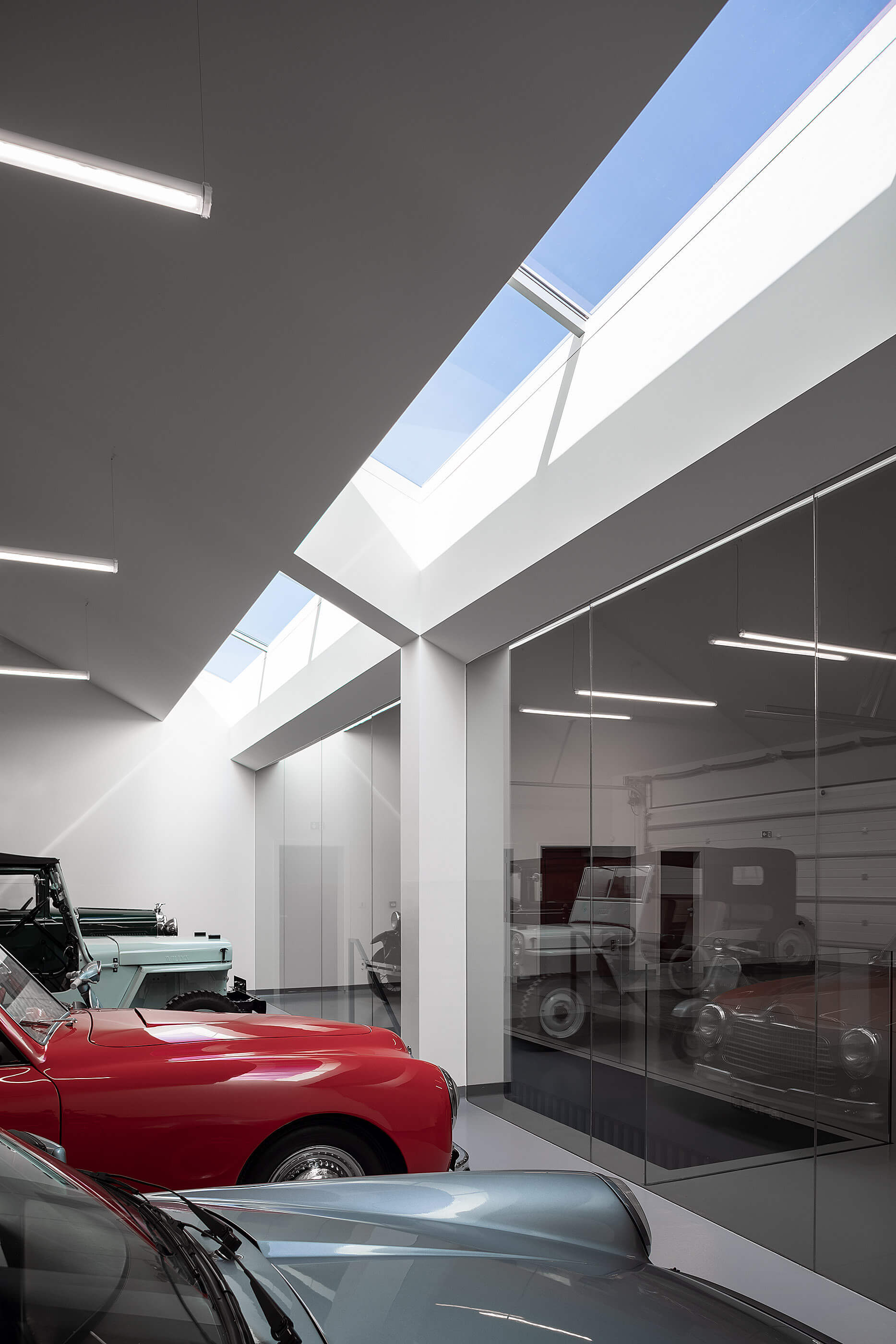 Interior da garagem com carros clássicos, claraboias e paredes brancas minimalistas. — Adega do Castanheirinho arquitetura João Albano Arquitecto em Águeda