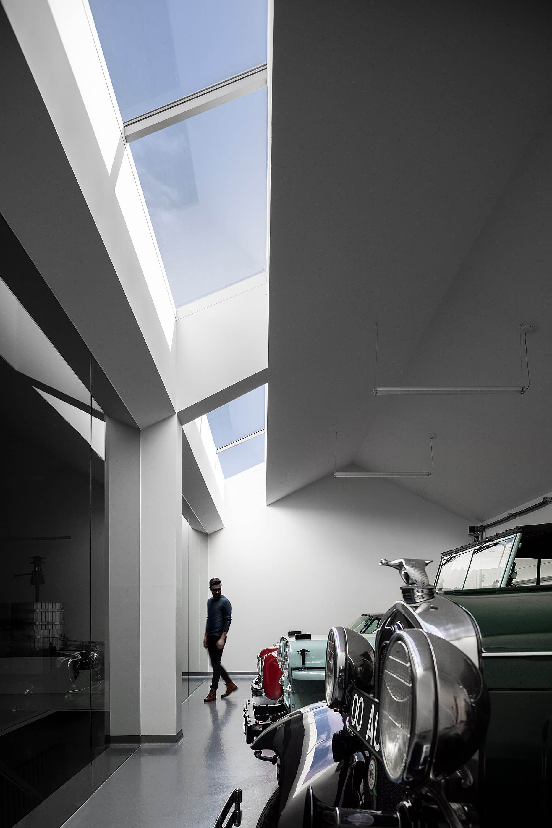Interior da garagem com carros clássicos, claraboias e homem a caminhar. — Adega do Castanheirinho arquitetura João Albano Arquitecto em Águeda