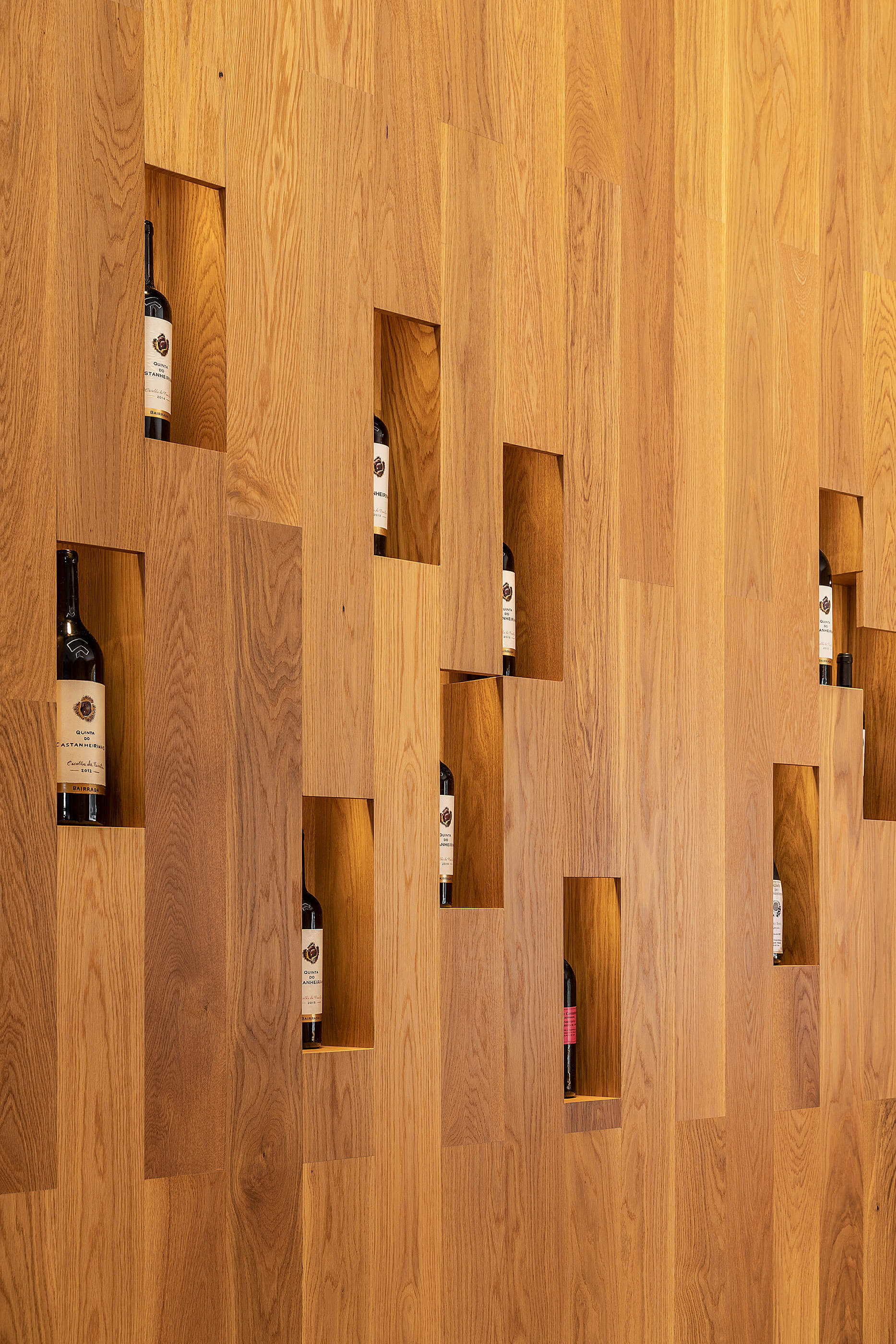 Parede de madeira clara com nichos irregulares para garrafas de vinho. — Adega do Castanheirinho arquitetura João Albano Arquitecto em Águeda