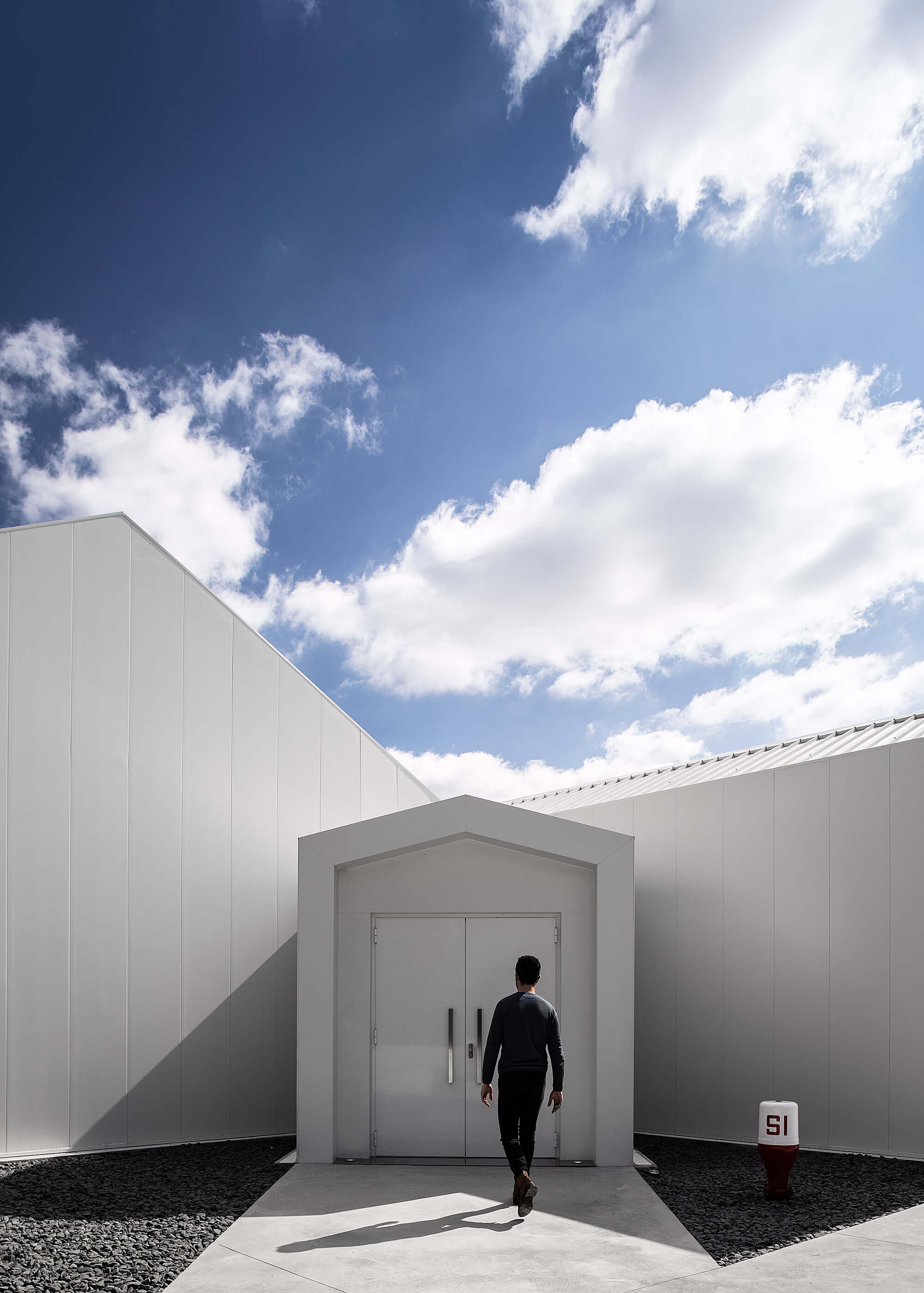 Homem a caminhar em direção à entrada principal da adega, com volumes brancos e céu azul. — Adega do Castanheirinho arquitetura João Albano Arquitecto em Águeda