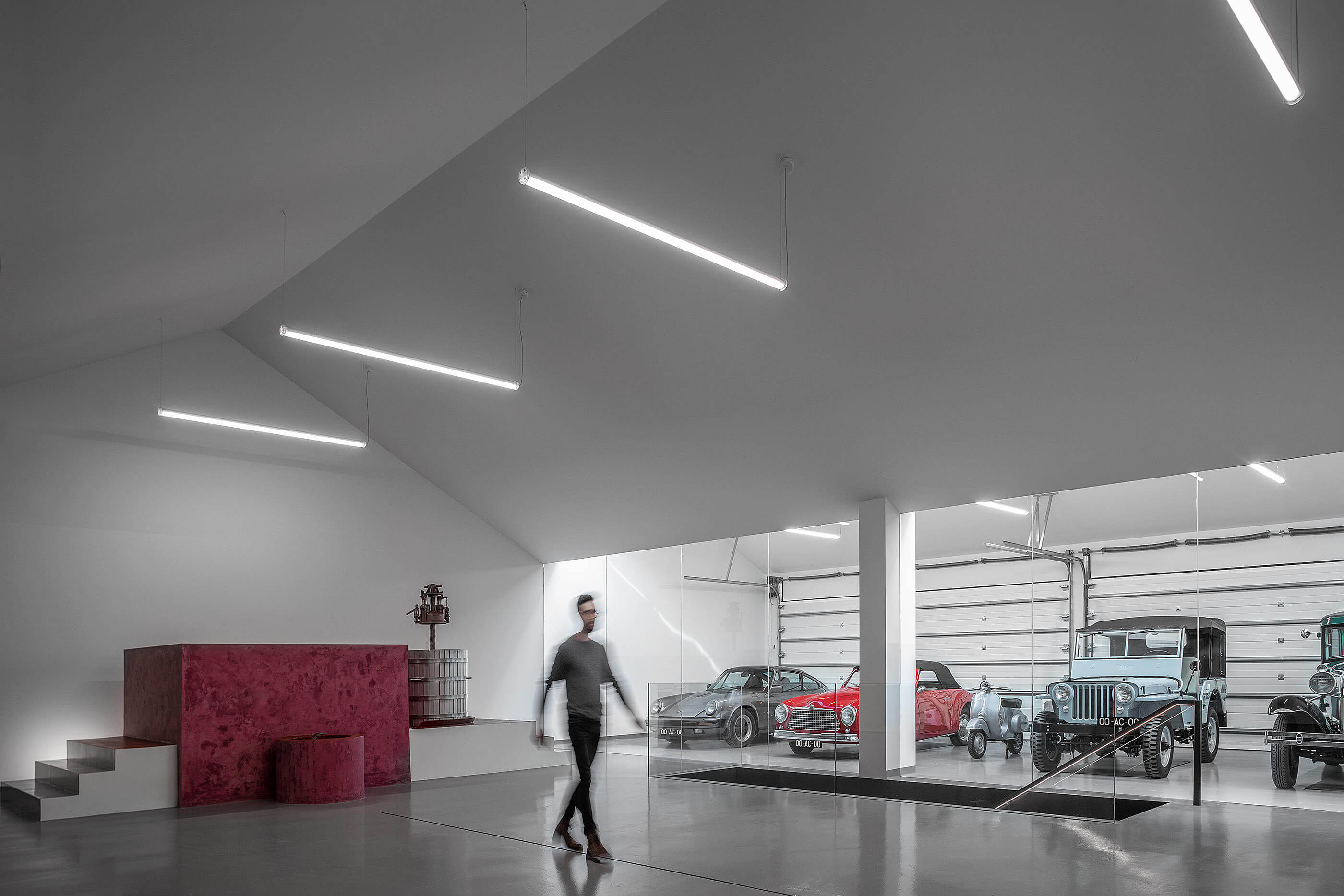 Espaço amplo com carros clássicos, prensa de vinho e homem a caminhar. — Adega do Castanheirinho arquitetura João Albano Arquitecto em Águeda