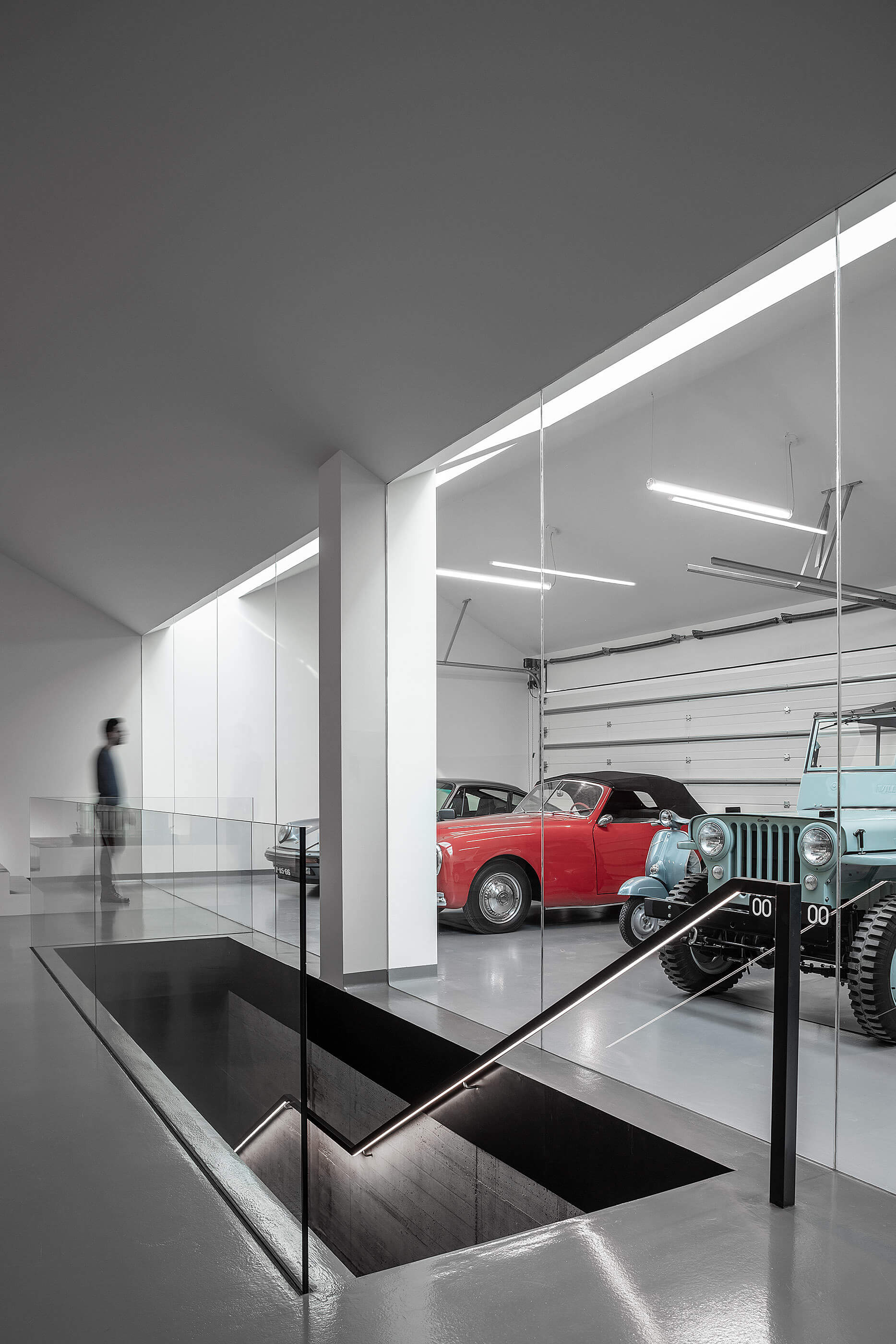 Garagem com carros clássicos, claraboias e escada de acesso ao piso inferior. — Adega do Castanheirinho arquitetura João Albano Arquitecto em Águeda