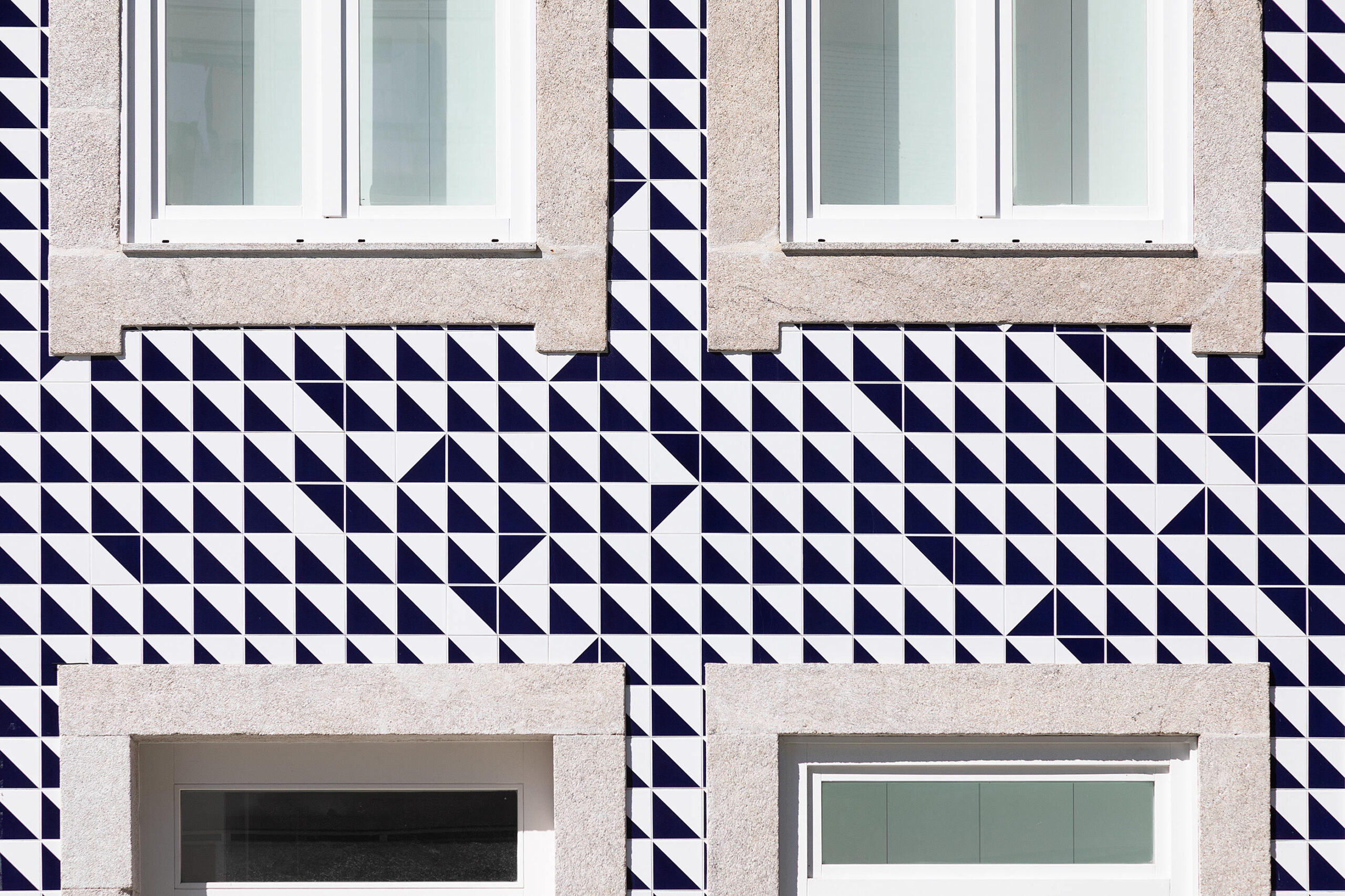 Fachada com azulejos decorativos azuis e brancos em padrão geométrico, emoldurando janelas de caixilharia branca. — Edifício Multifamiliar Alegria arquitetura MiMool Arquitectura & Interiores em Porto