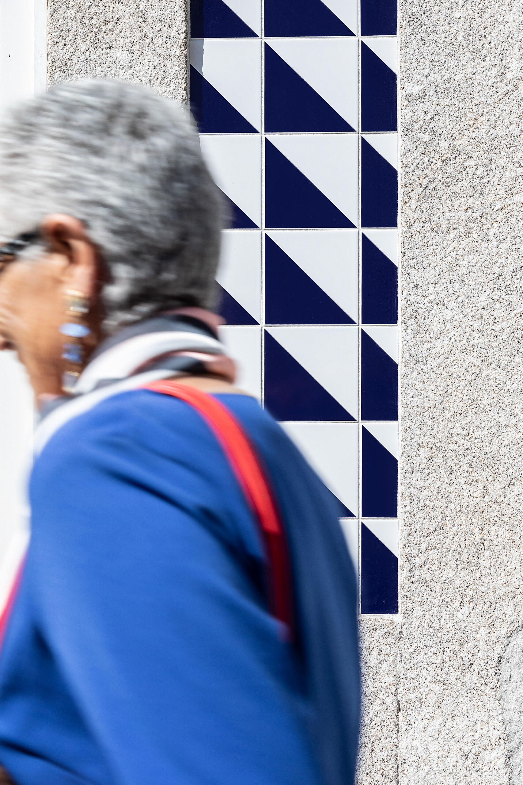 Detalhe da fachada com azulejos azuis e brancos, emoldurando uma janela. Pessoa desfocada em primeiro plano. — Edifício Multifamiliar Alegria arquitetura MiMool Arquitectura & Interiores em Porto
