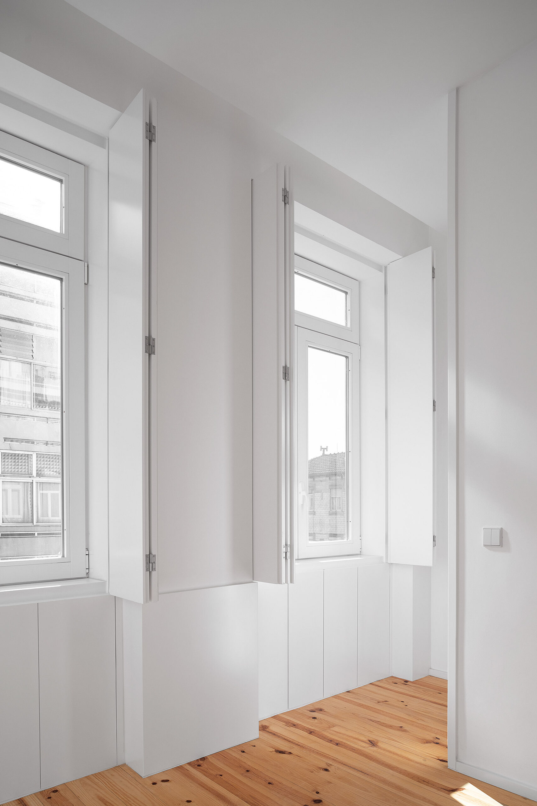 Quarto com janelas de madeira branca e portadas, chão em madeira clara e paredes brancas. Estilo minimalista. — Edifício Multifamiliar Alegria arquitetura MiMool Arquitectura & Interiores em Porto