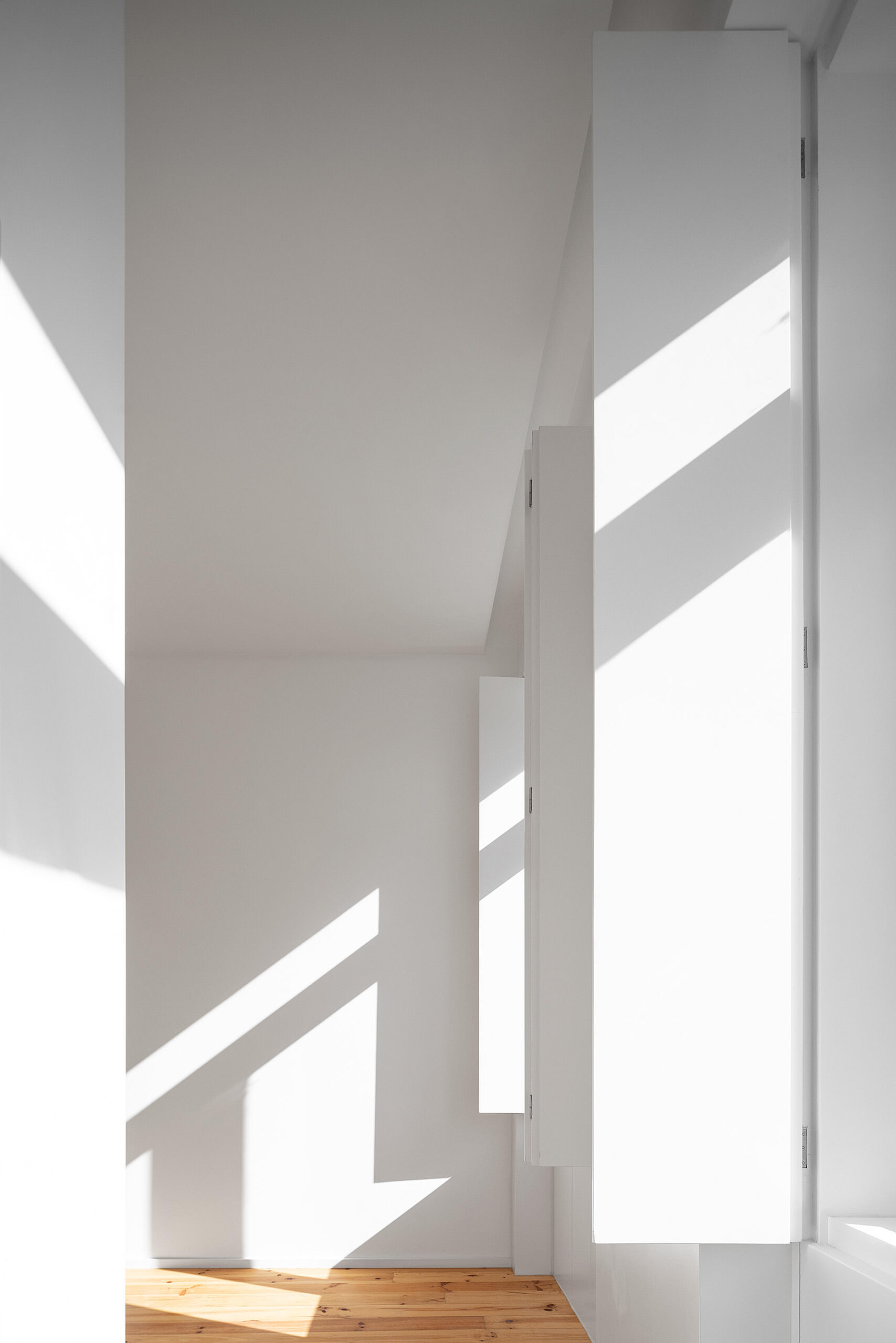 Quarto inundado de luz natural, com portadas brancas e chão de madeira. Minimalismo e luminosidade. — Edifício Multifamiliar Alegria arquitetura MiMool Arquitectura & Interiores em Porto