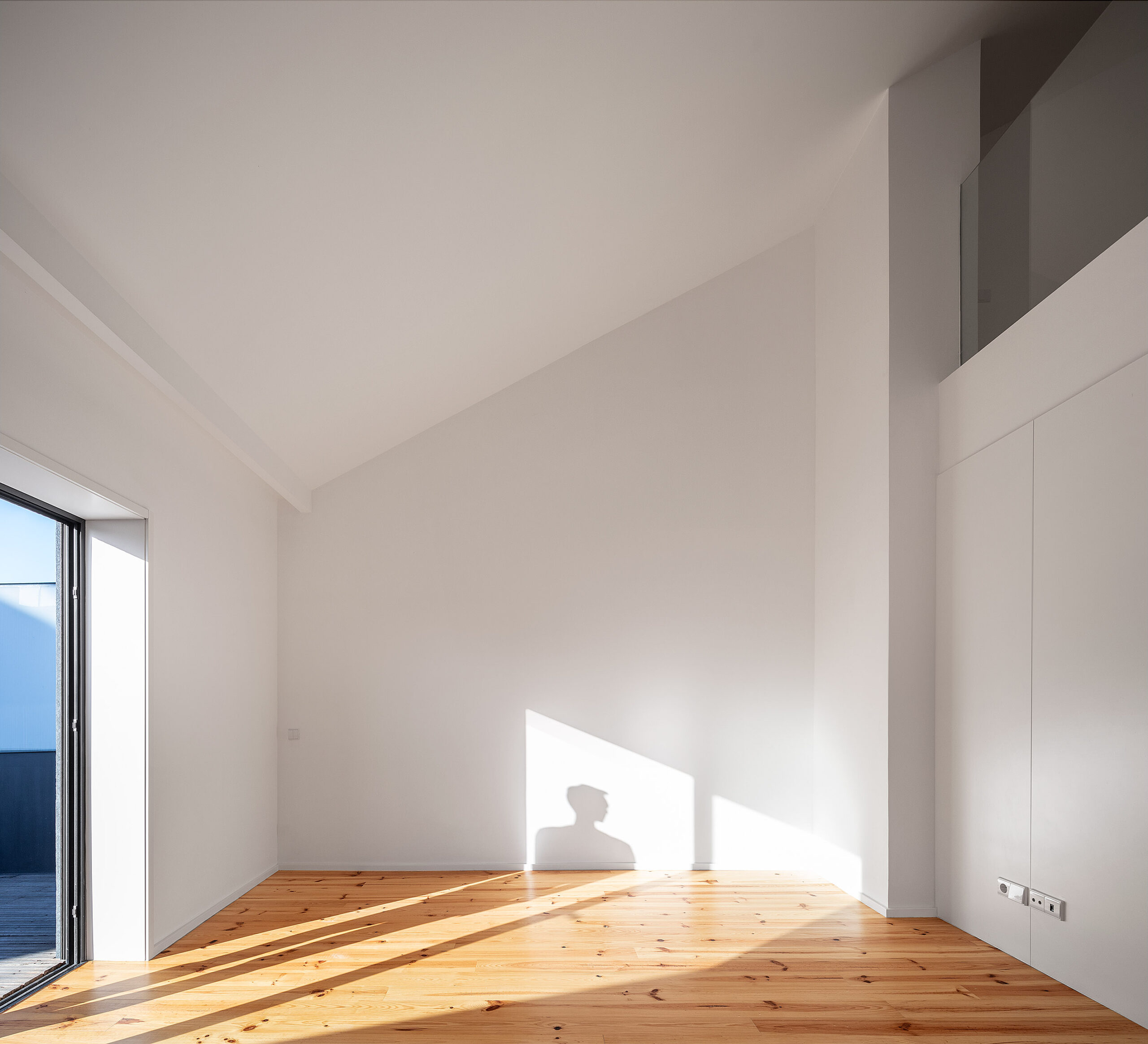 Quarto amplo com pé direito alto, chão de madeira clara, paredes brancas e porta de acesso ao terraço. — Edifício Multifamiliar Alegria arquitetura MiMool Arquitectura & Interiores em Porto