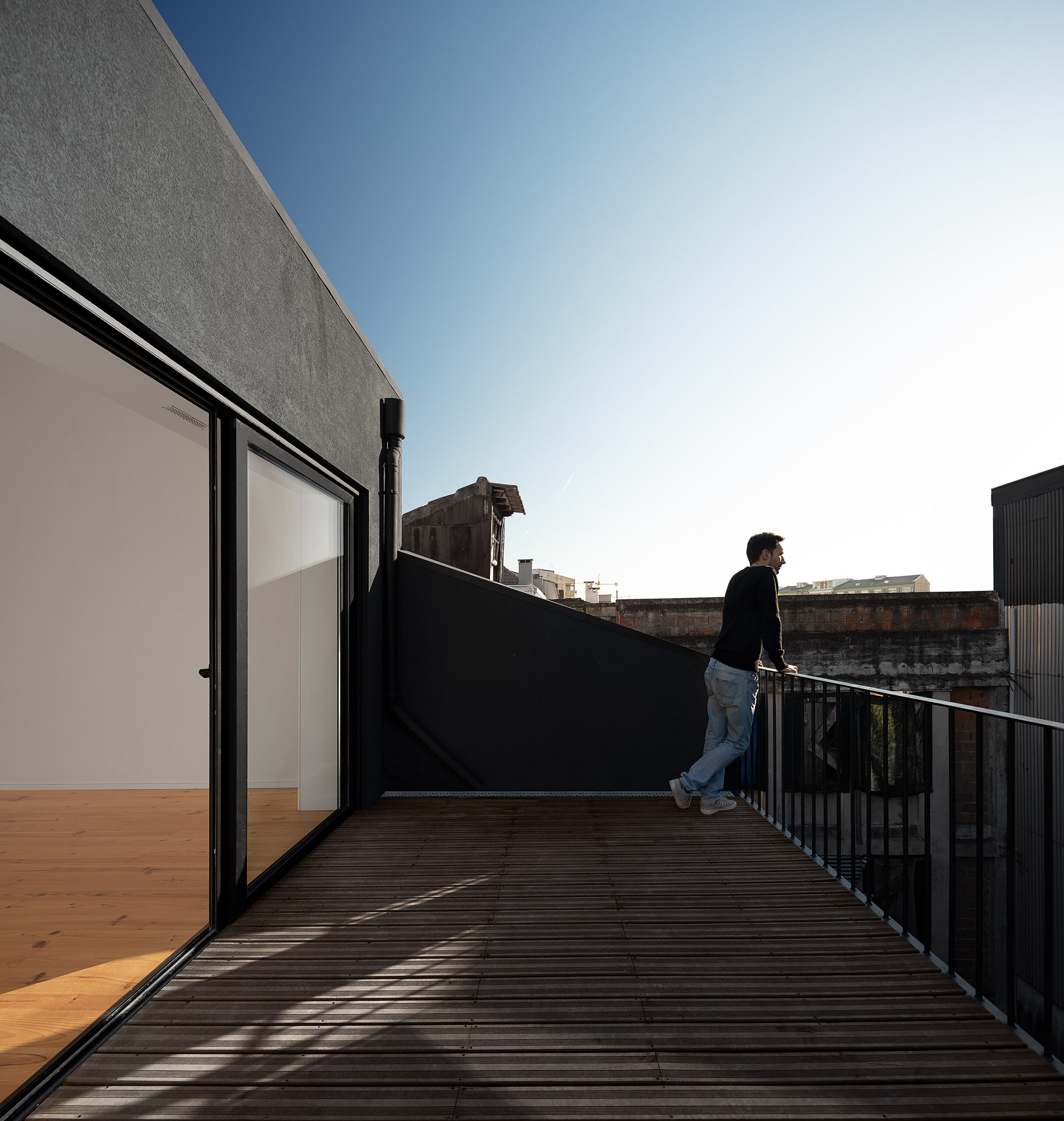 Terraço com deck de madeira escura, guarda-corpo metálico preto e vista para a cidade do Porto. — Edifício Multifamiliar Alegria arquitetura MiMool Arquitectura & Interiores em Porto