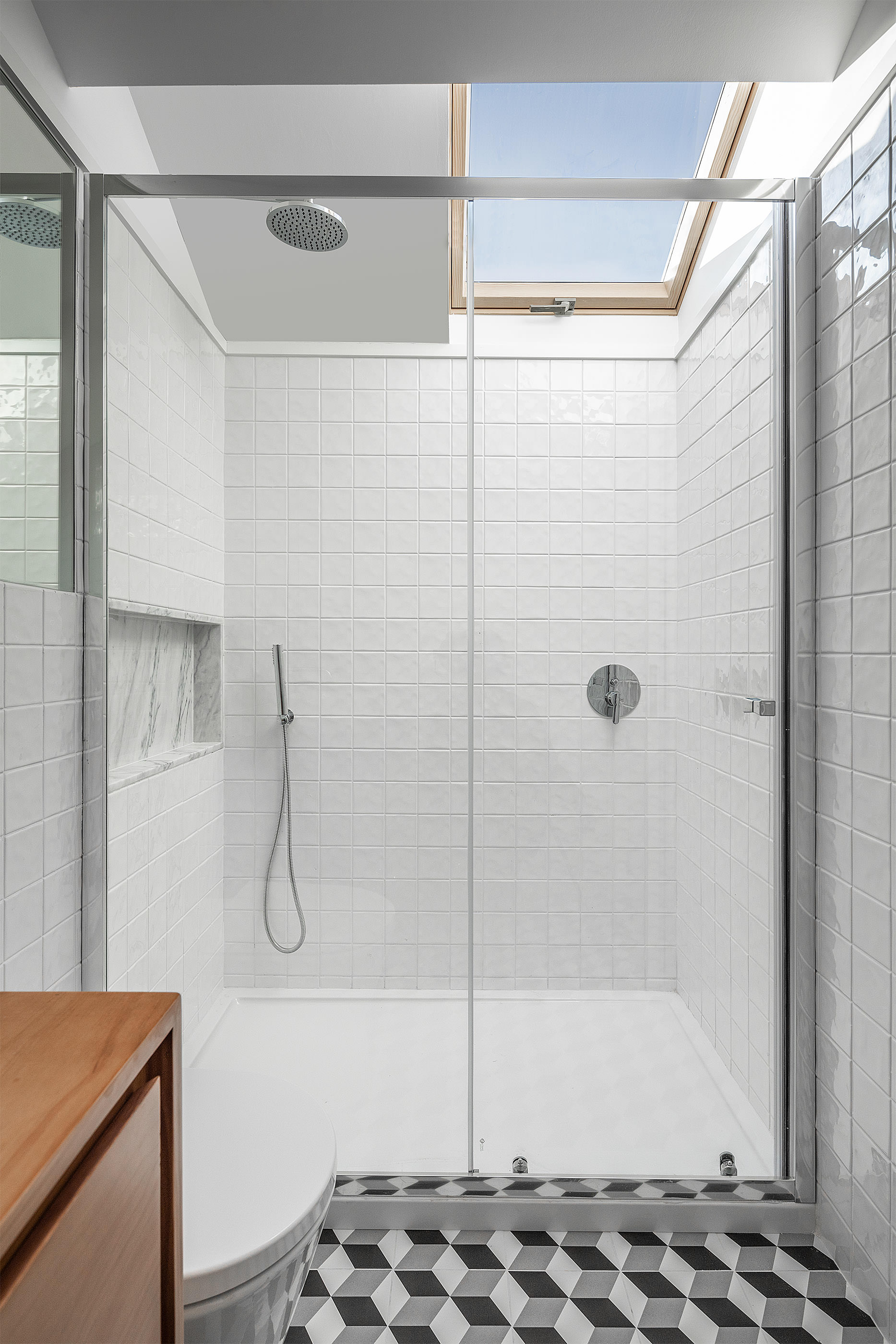 Casa de banho com duche em vidro, revestimento em azulejo branco, claraboia e pavimento geométrico preto e branco. — Edifício Multifamiliar Alegria arquitetura MiMool Arquitectura & Interiores em Porto