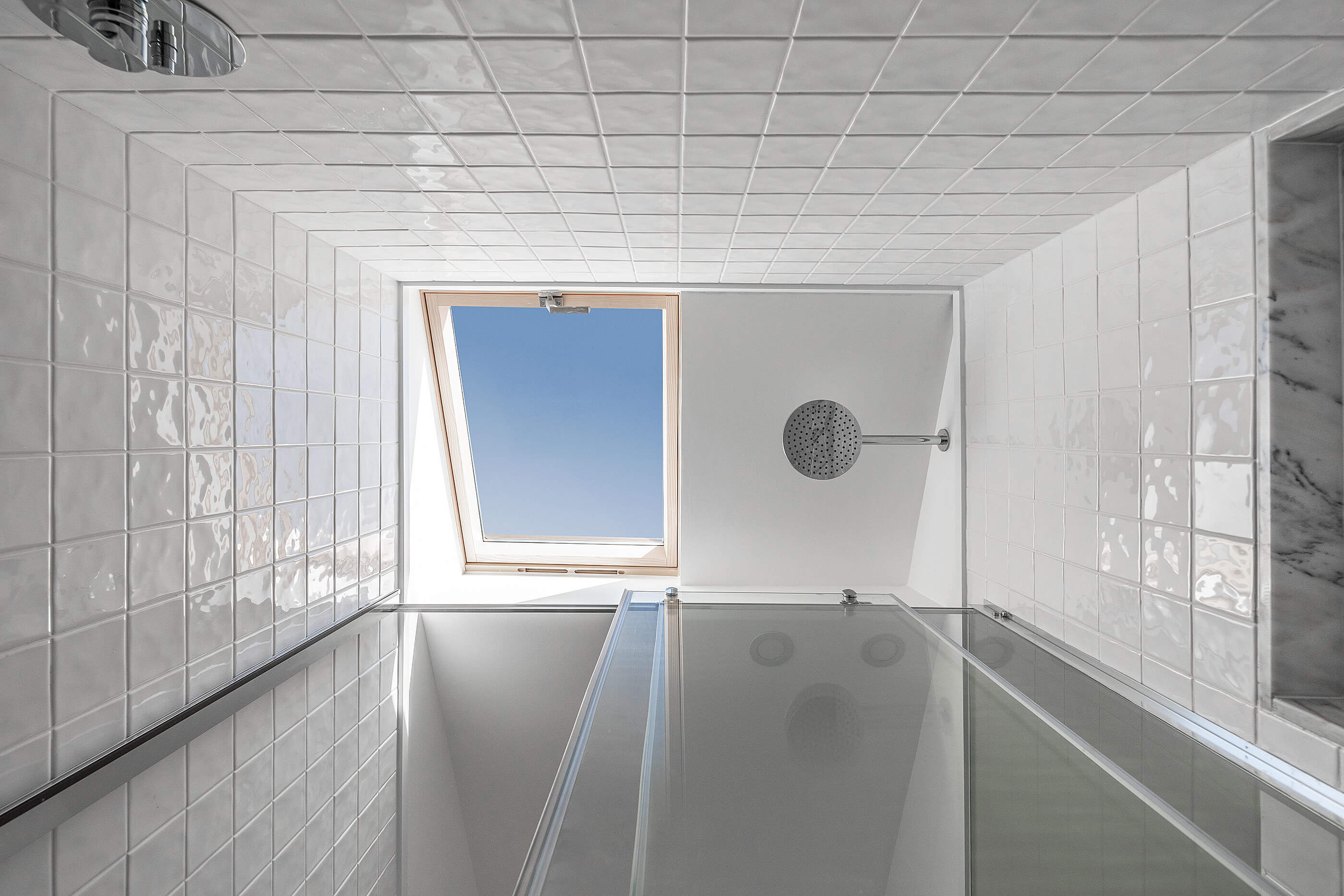 Casa de banho com duche em vidro, revestimento em azulejo branco, claraboia e chuveiro de grandes dimensões. — Edifício Multifamiliar Alegria arquitetura MiMool Arquitectura & Interiores em Porto