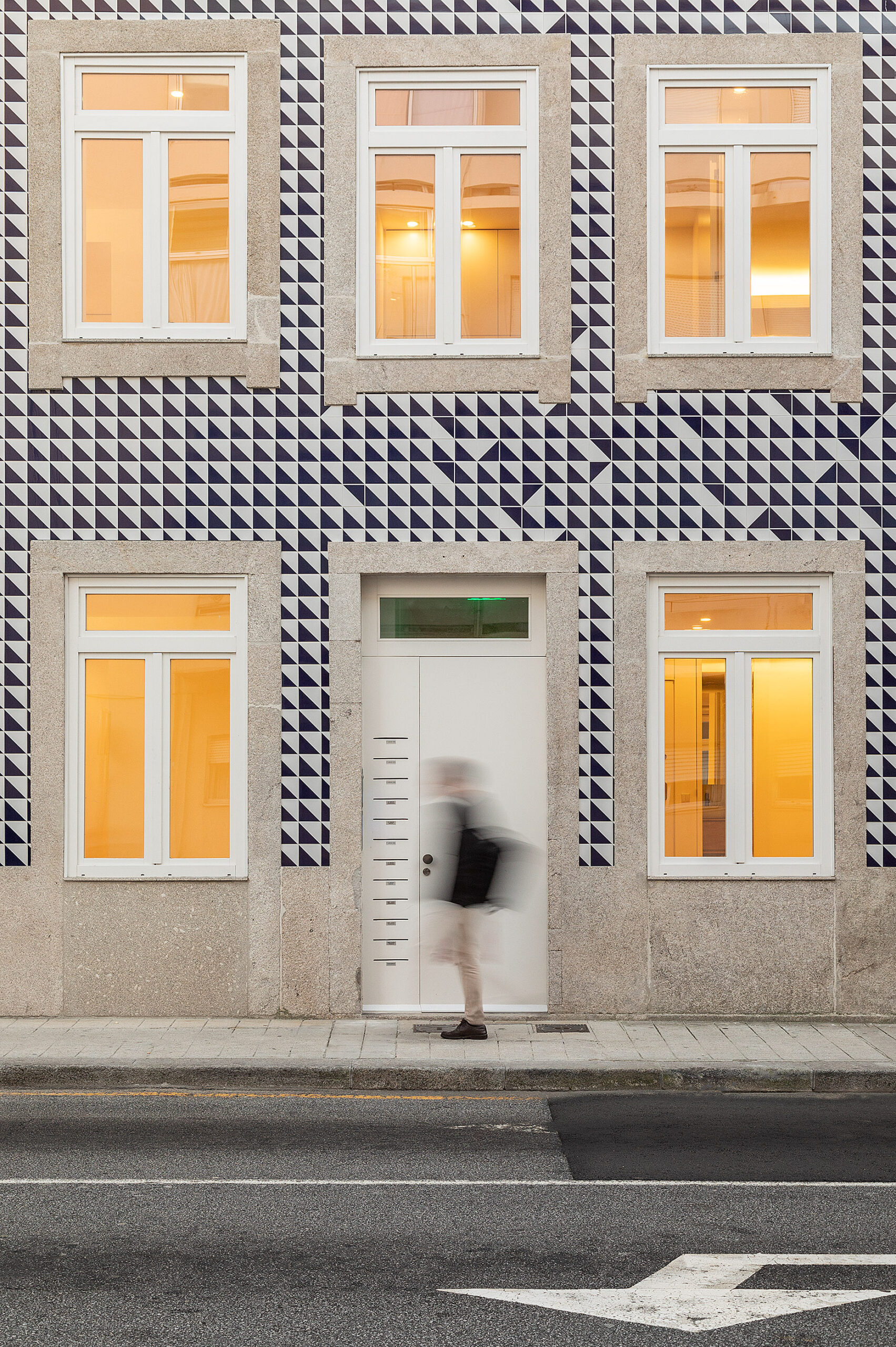 Detalhe da fachada principal com azulejos azuis e brancos, janelas brancas e porta de entrada. Pessoa desfocada. — Edifício Multifamiliar Alegria arquitetura MiMool Arquitectura & Interiores em Porto