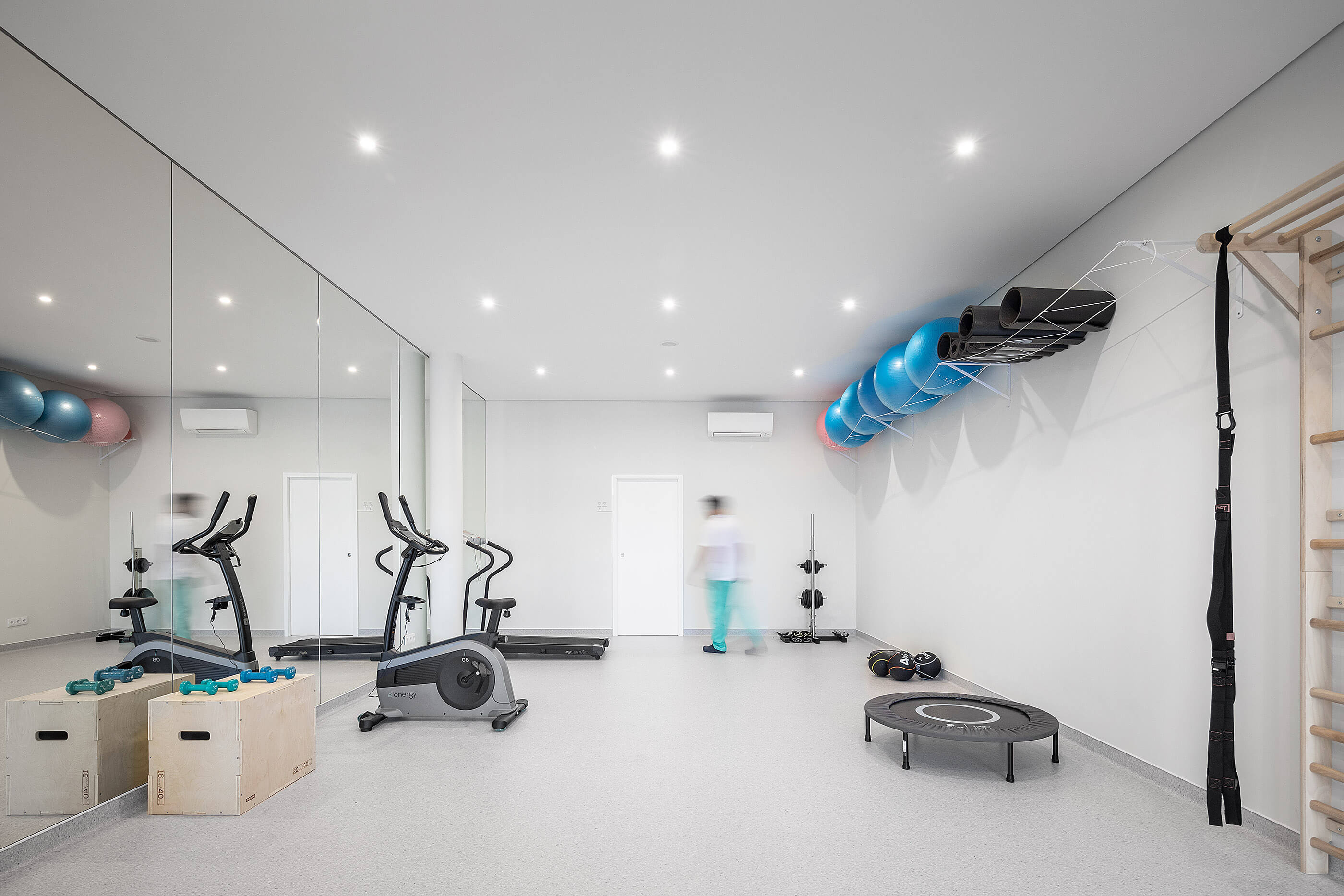 Sala de exercício com espelhos amplos, equipamentos diversos e pavimento cinza; ambiente luminoso. — Clínica de Fisioterapia Mar Saúde arquitetura Hinterland Architecture Studio em Vila Nova de Gaia
