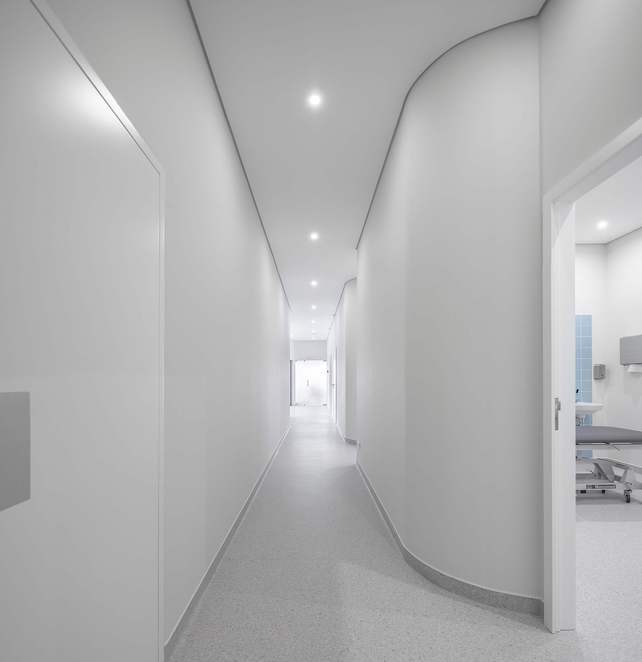 Corredor branco com portas laterais e pavimento cinza; iluminação embutida e ambiente clean. — Clínica de Fisioterapia Mar Saúde arquitetura Hinterland Architecture Studio em Vila Nova de Gaia