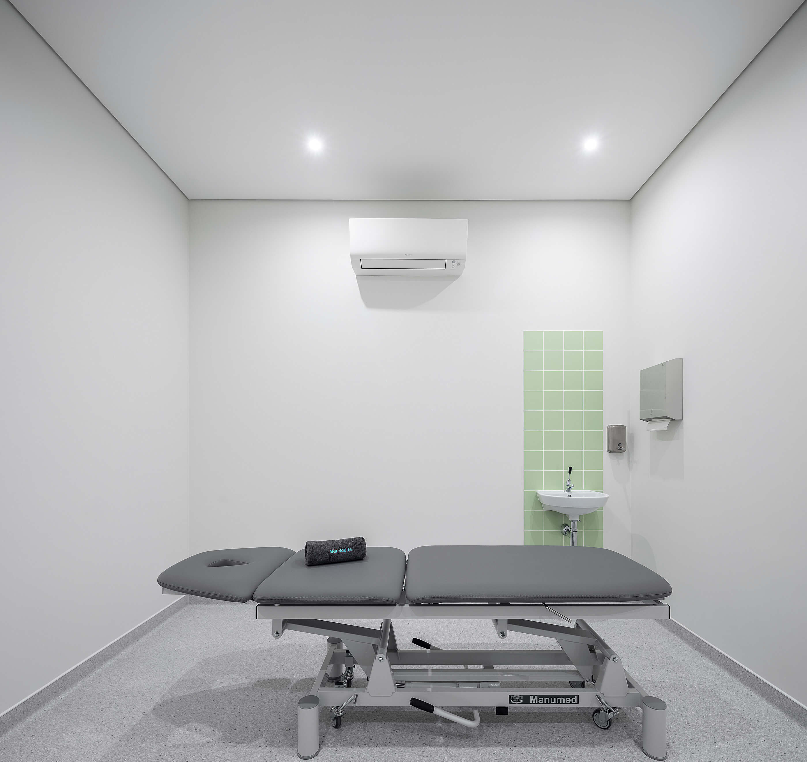 Sala de tratamento com marquesa cinza, lavatório com azulejos verdes e pavimento cinza; ambiente minimalista. — Clínica de Fisioterapia Mar Saúde arquitetura Hinterland Architecture Studio em Vila Nova de Gaia