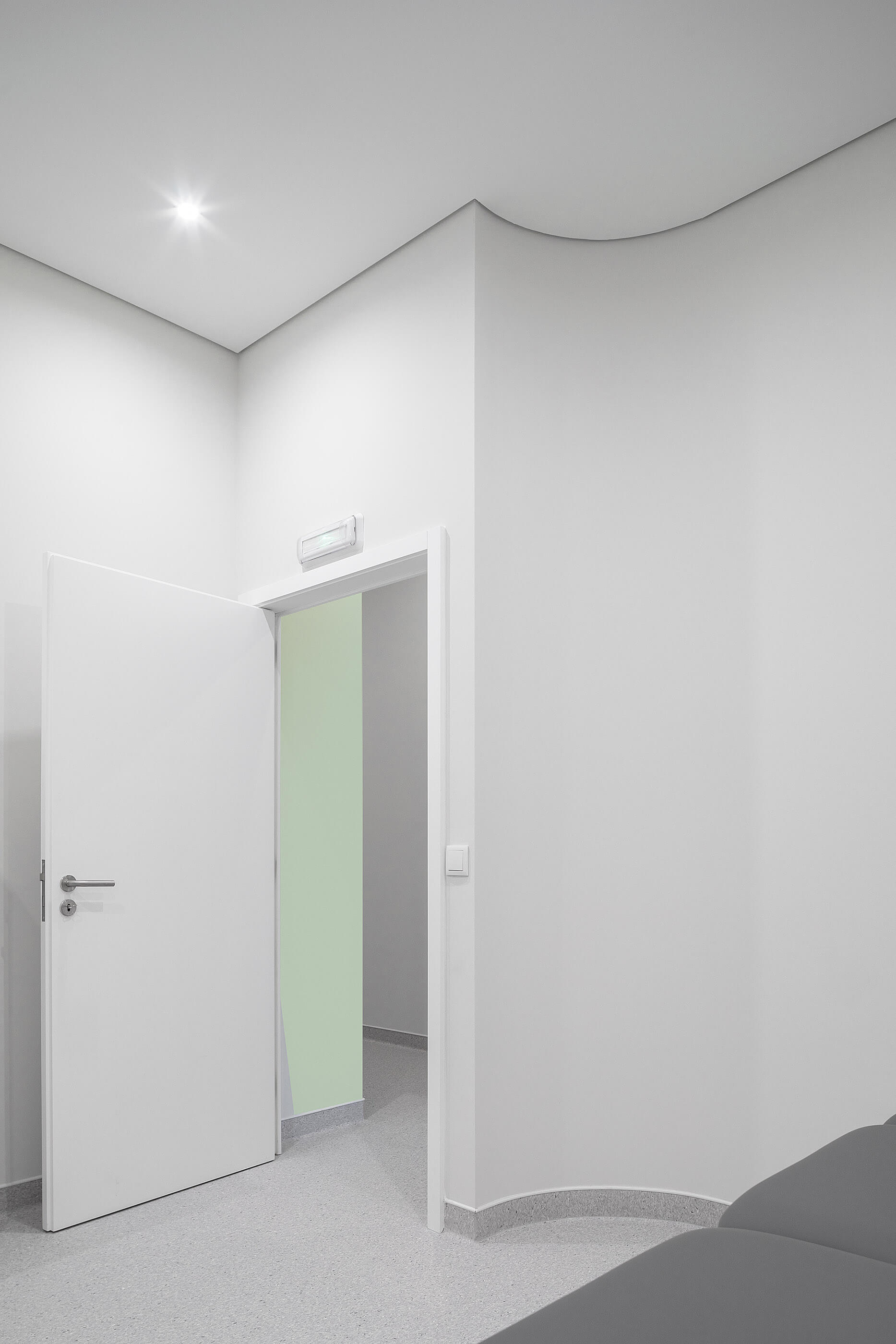 Detalhe de porta aberta para sala com parede verde; pavimento cinza e paredes brancas. — Clínica de Fisioterapia Mar Saúde arquitetura Hinterland Architecture Studio em Vila Nova de Gaia