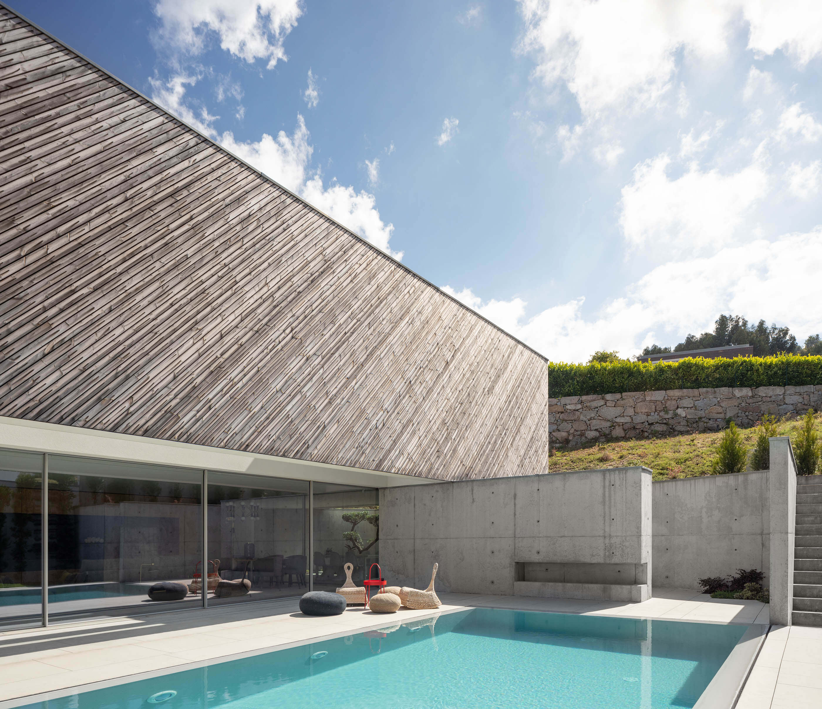 Piscina exterior da Casa A, com fachada em madeira inclinada e zona de estar. Estilo moderno e minimalista. — Casa A arquitetura REM'A Arquitectos em Portugal