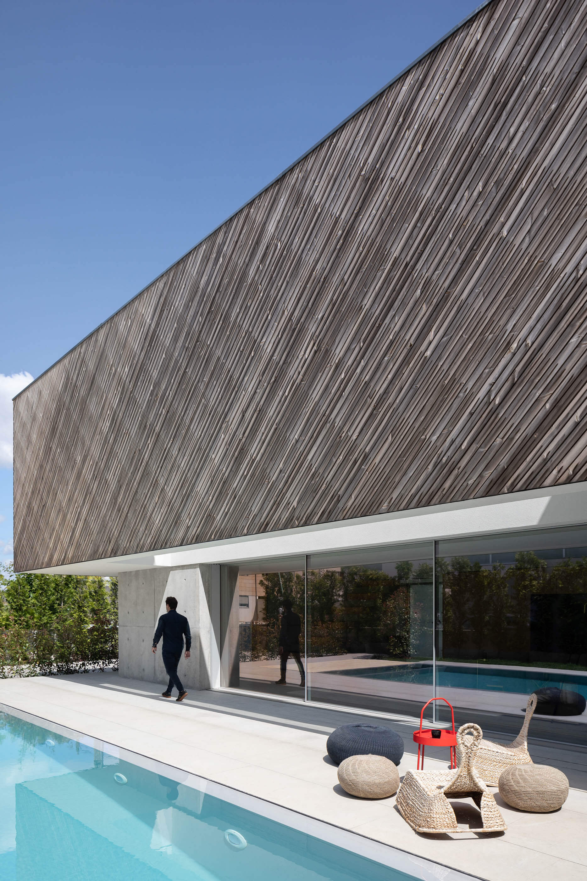 Exterior da Casa A com revestimento em madeira, piscina e espreguiçadeiras de vime. — Casa A arquitetura REM'A Arquitectos em Portugal