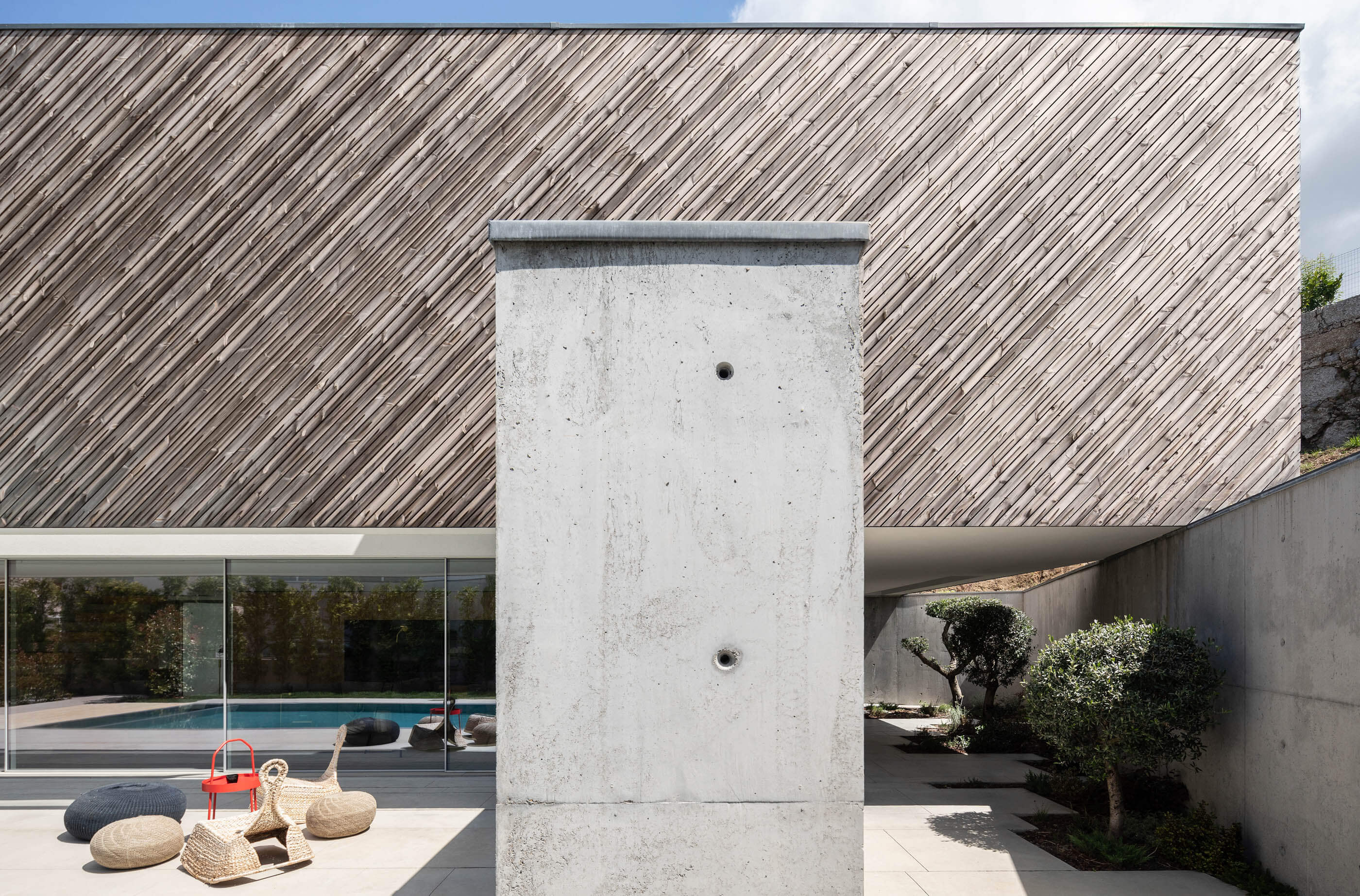 Pátio exterior da Casa A com parede de betão aparente, revestimento em madeira e mobiliário de jardim. — Casa A arquitetura REM'A Arquitectos em Portugal
