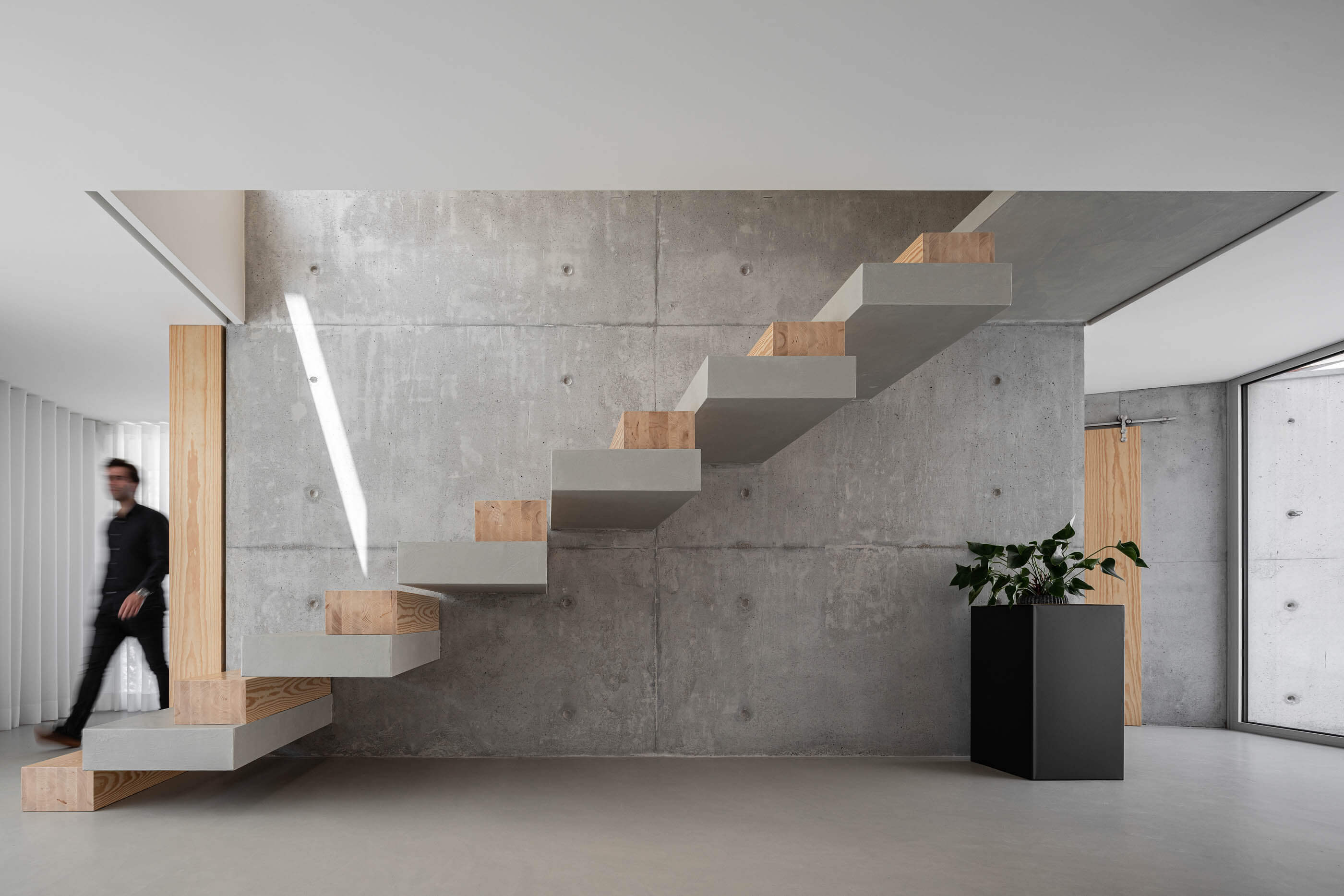 Escada interior flutuante em betão e madeira, com parede em betão aparente e iluminação natural. — Casa A arquitetura REM'A Arquitectos em Portugal