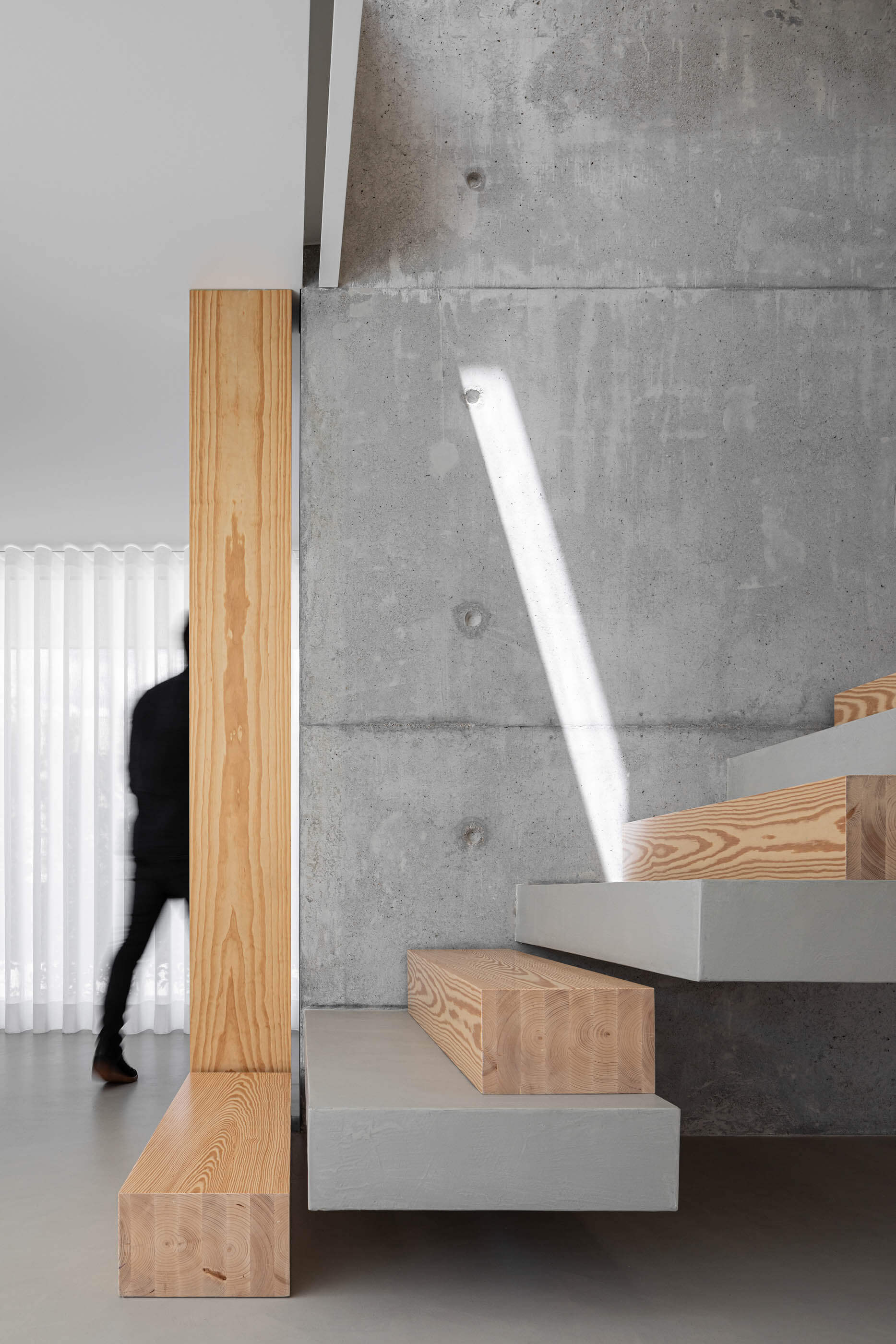 Detalhe da escada flutuante em betão e madeira, com parede em betão aparente e luz natural. — Casa A arquitetura REM'A Arquitectos em Portugal