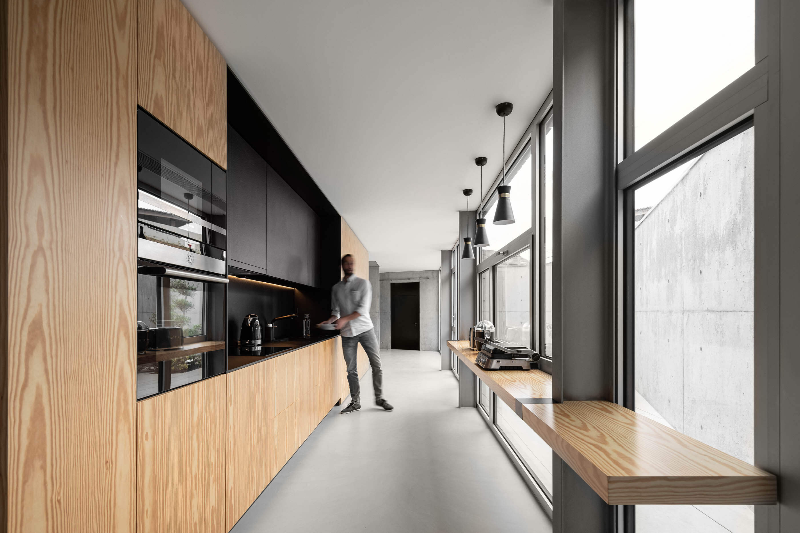 Cozinha moderna com armários em madeira clara, bancada preta e grandes janelas com vista exterior. — Casa A arquitetura REM'A Arquitectos em Portugal