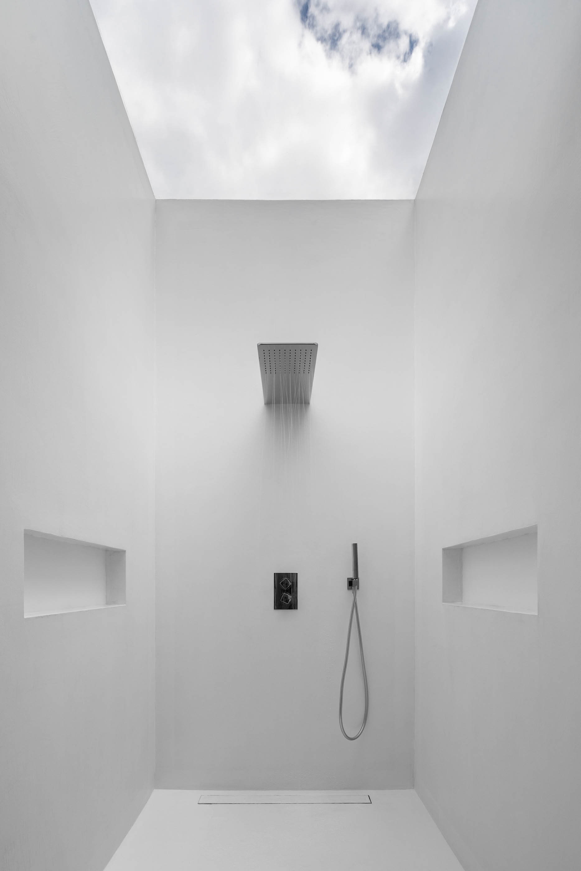 Duche minimalista branco com chuveiro de teto e nichos nas paredes, sob uma claraboia. — Casa A arquitetura REM'A Arquitectos em Portugal