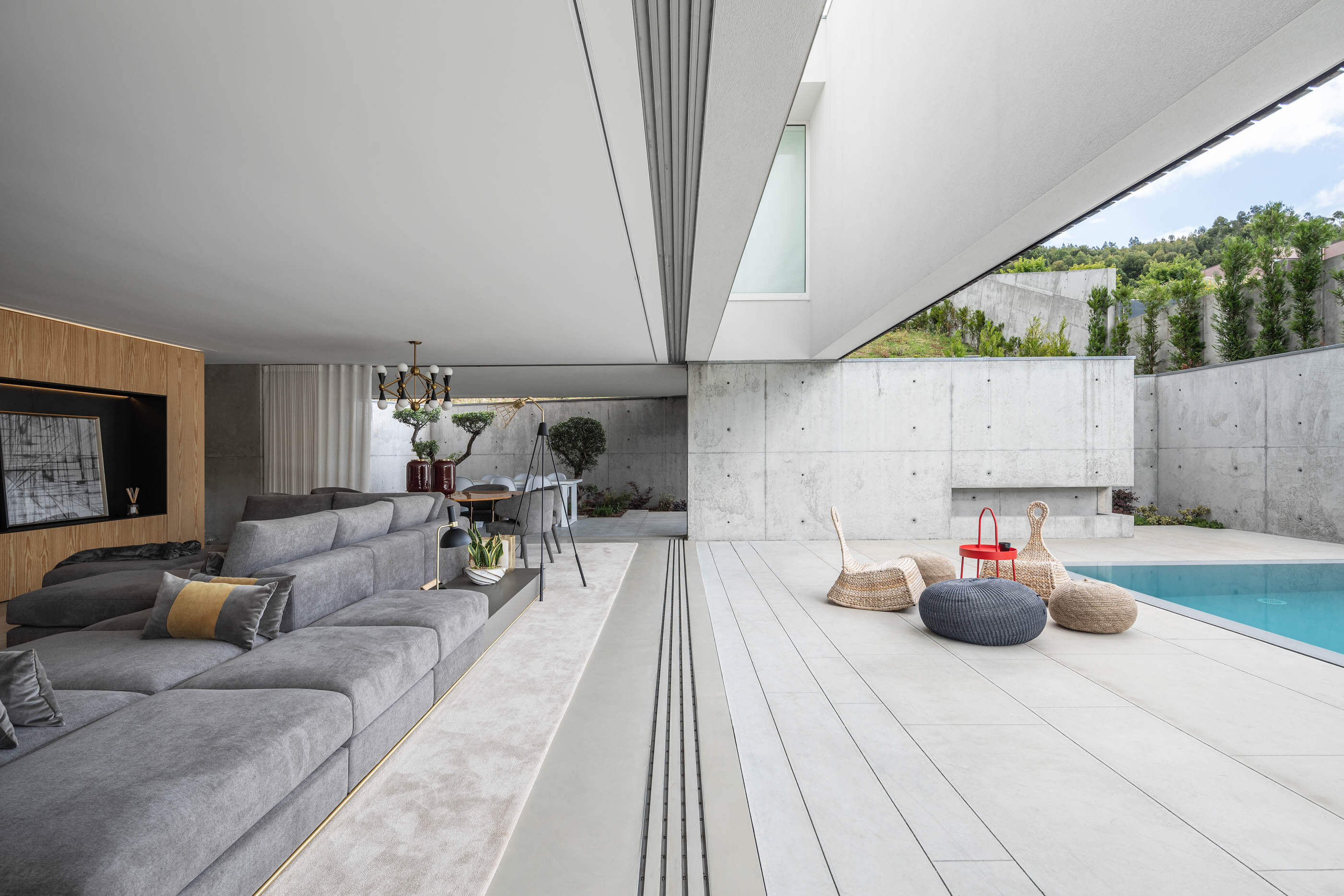 Sala de estar com sofá cinzento, zona de refeições e pátio exterior com piscina. — Casa A arquitetura REM'A Arquitectos em Portugal