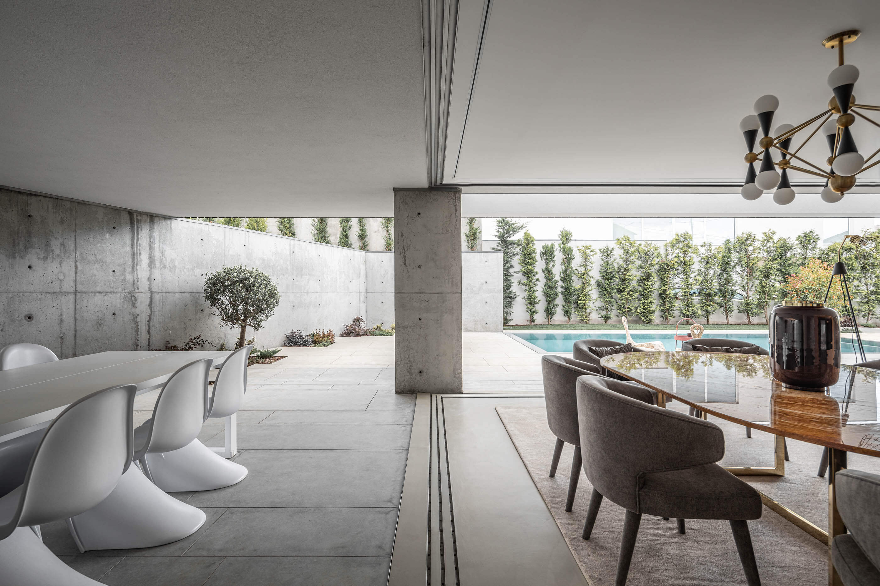 Sala de jantar com mesa de madeira e cadeiras modernas, com vista para o pátio exterior e piscina. — Casa A arquitetura REM'A Arquitectos em Portugal