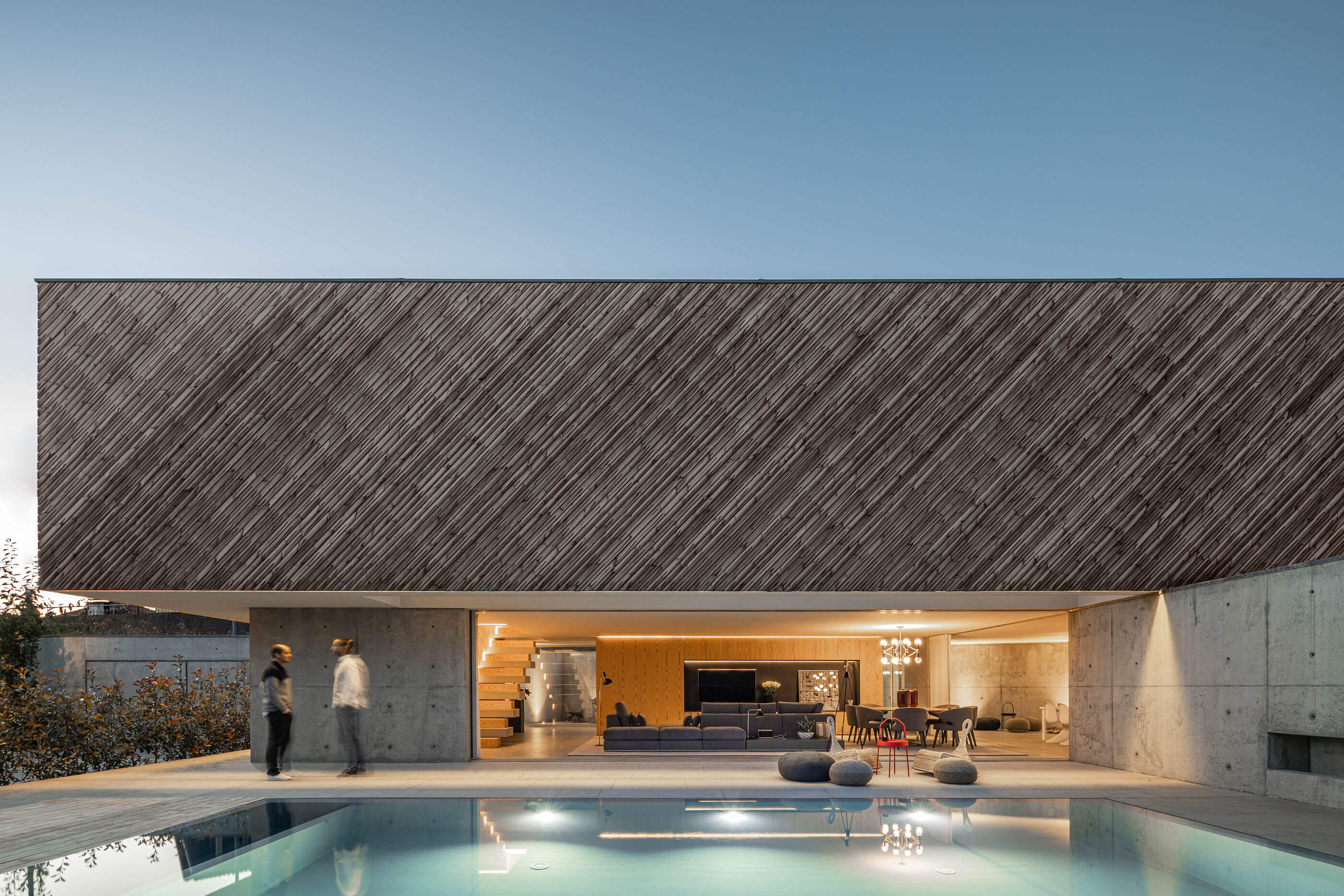 Vista noturna da Casa A com piscina iluminada, fachada em madeira e interior iluminado. — Casa A arquitetura REM'A Arquitectos em Portugal
