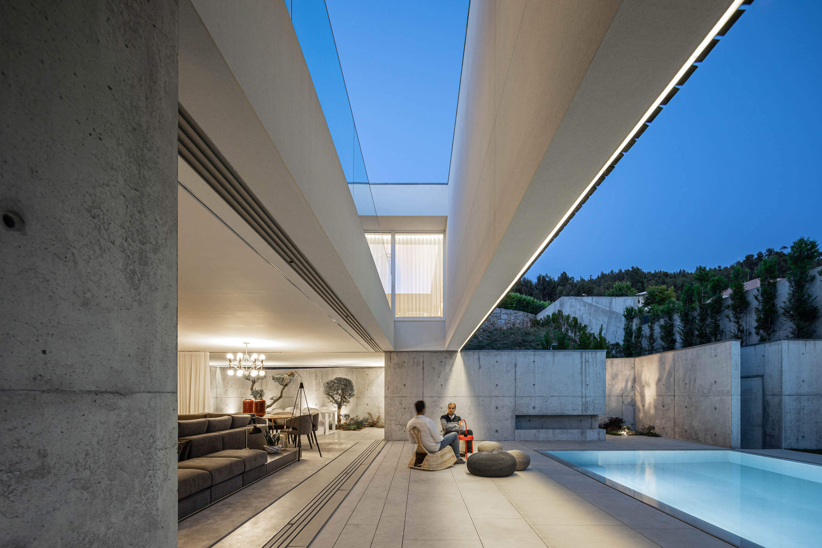 Vista noturna da Casa A com piscina iluminada, zona de estar exterior e interior iluminado. — Casa A arquitetura REM'A Arquitectos em Portugal