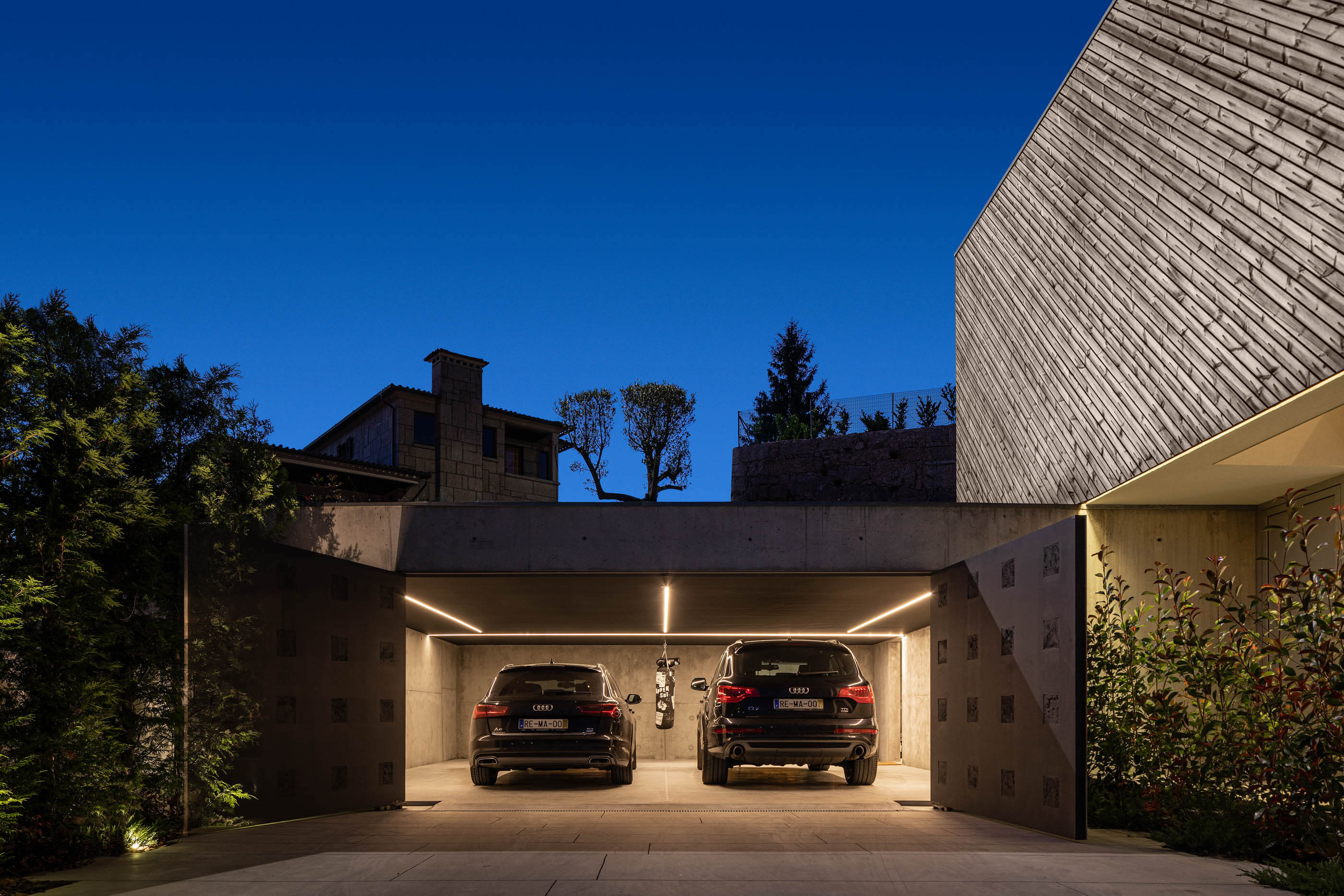 Garagem da Casa A com dois carros estacionados e iluminação embutida. — Casa A arquitetura REM'A Arquitectos em Portugal