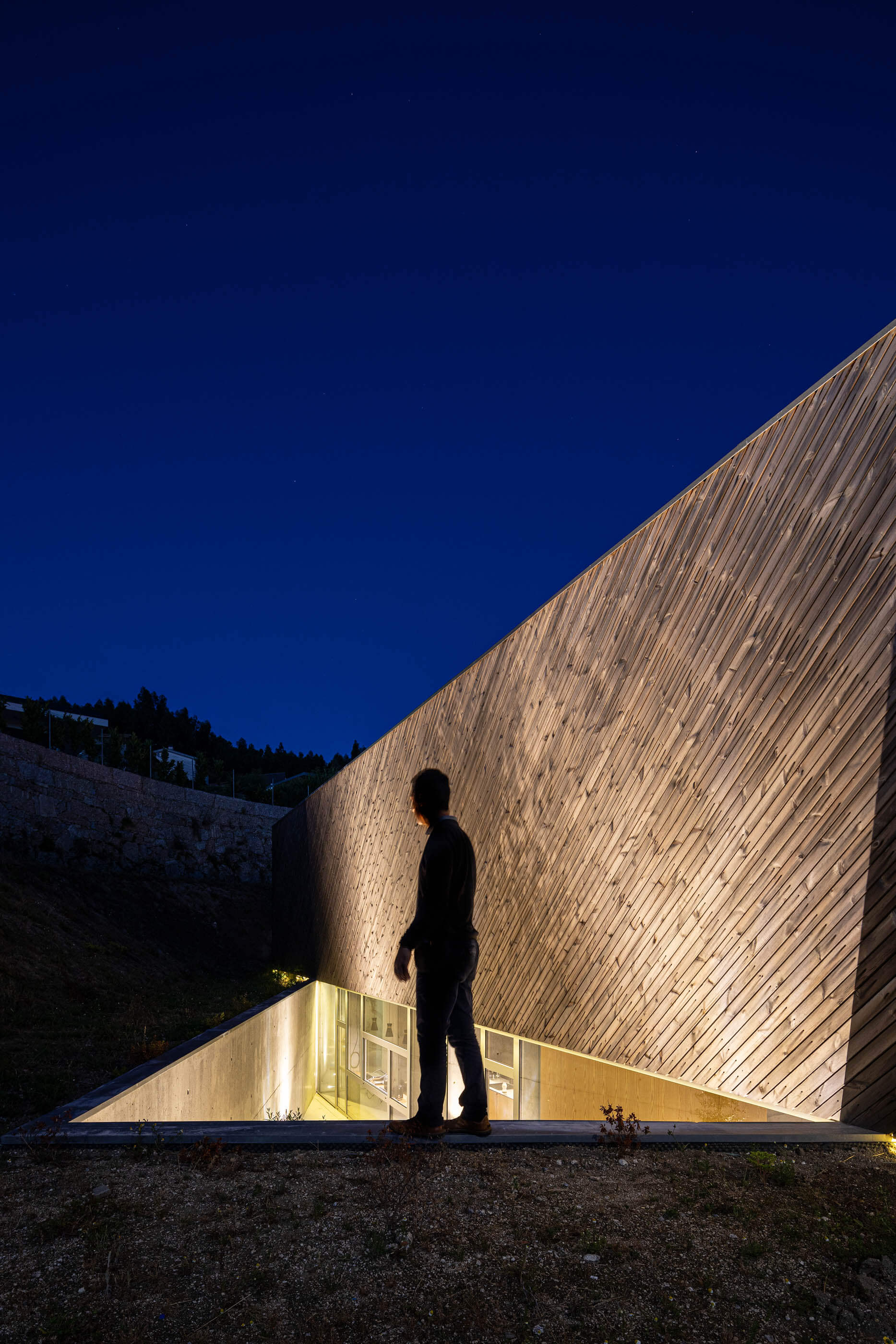 Vista noturna da fachada em madeira da Casa A, com iluminação interior e exterior. — Casa A arquitetura REM'A Arquitectos em Portugal