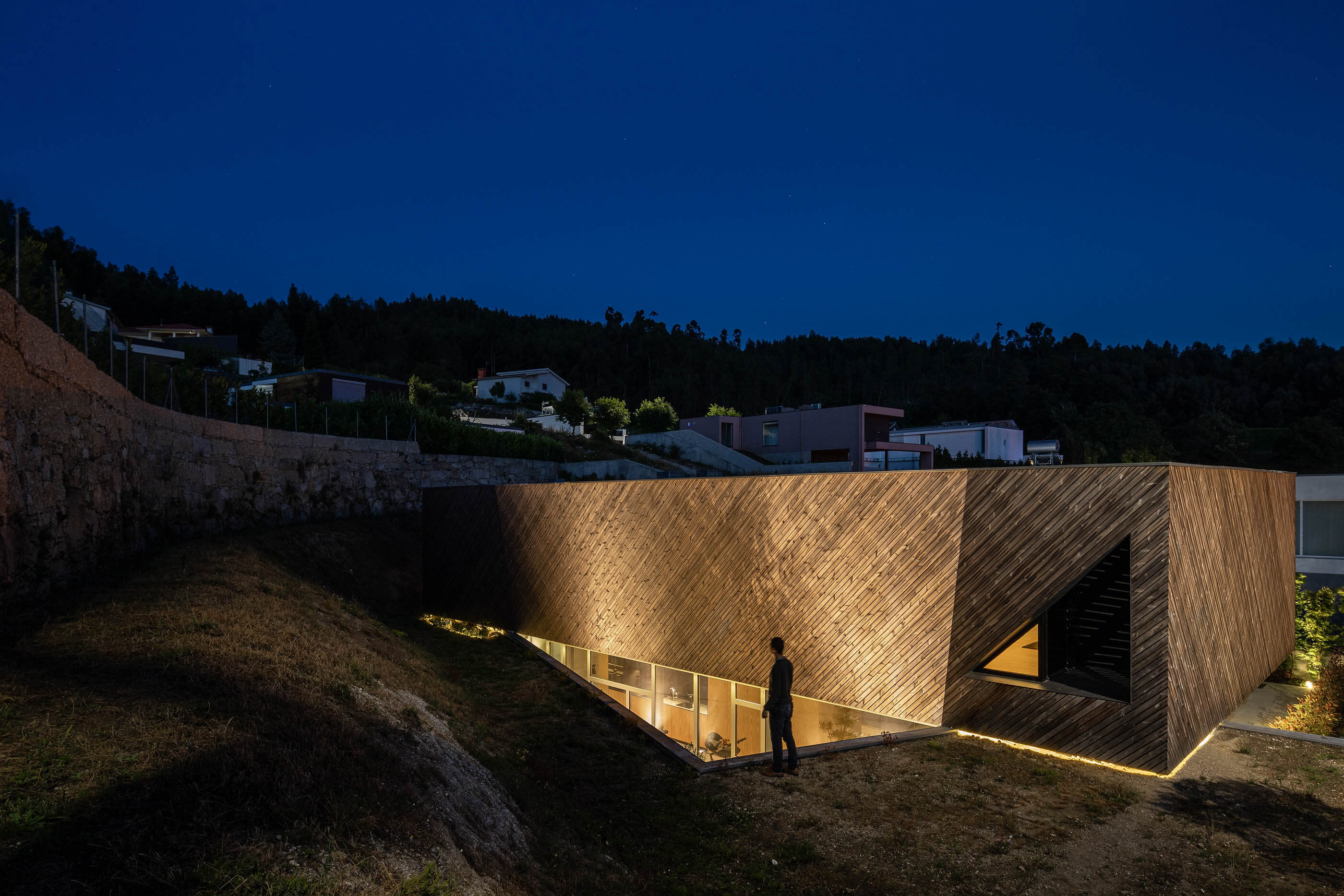 Vista noturna da Casa A com fachada em madeira, iluminação exterior e jardim. — Casa A arquitetura REM'A Arquitectos em Portugal