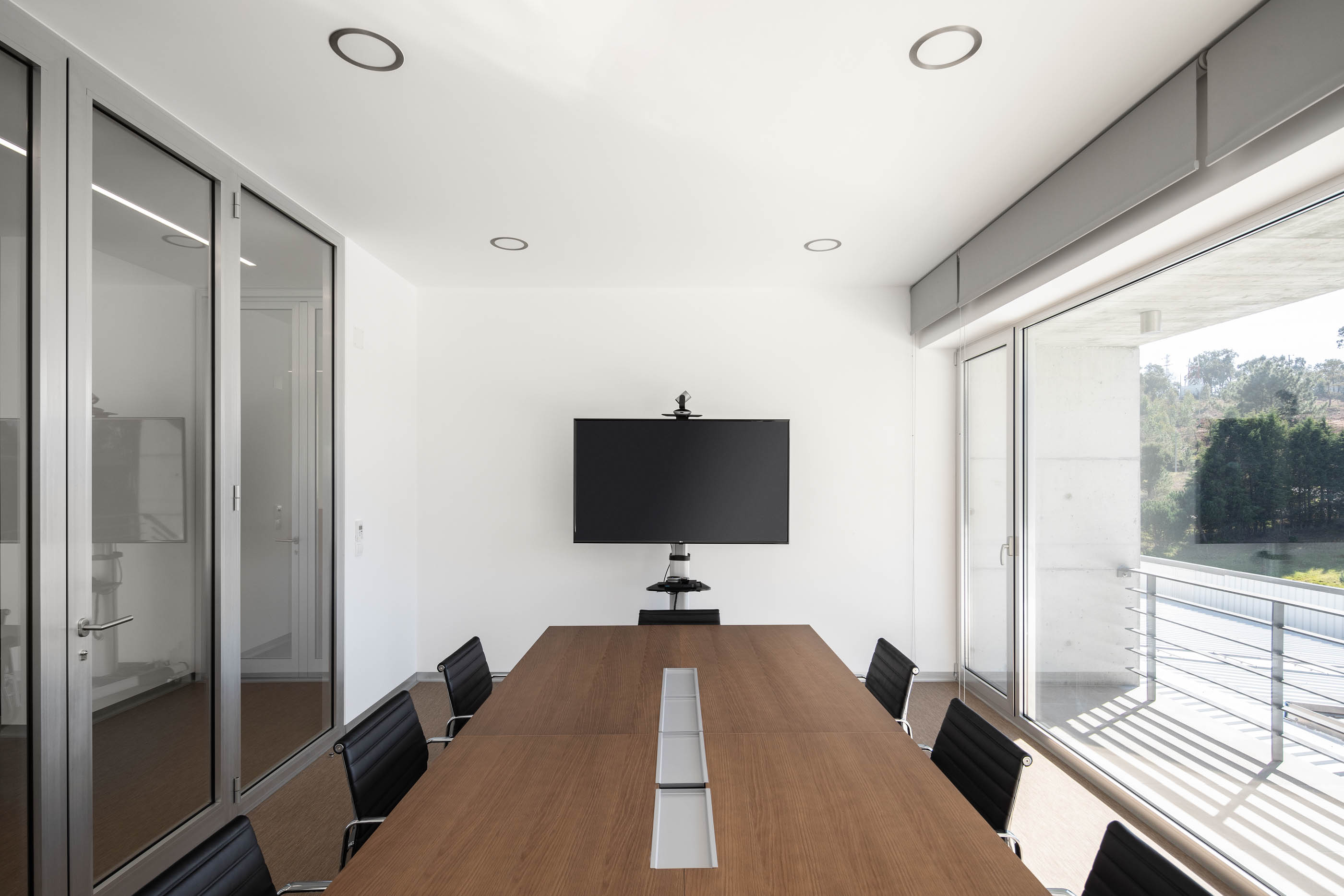 Sala de reuniões moderna com mesa de madeira, cadeiras pretas e luz natural abundante. — Edifício Sede PRF arquitetura Impare Arquitectura em Portugal