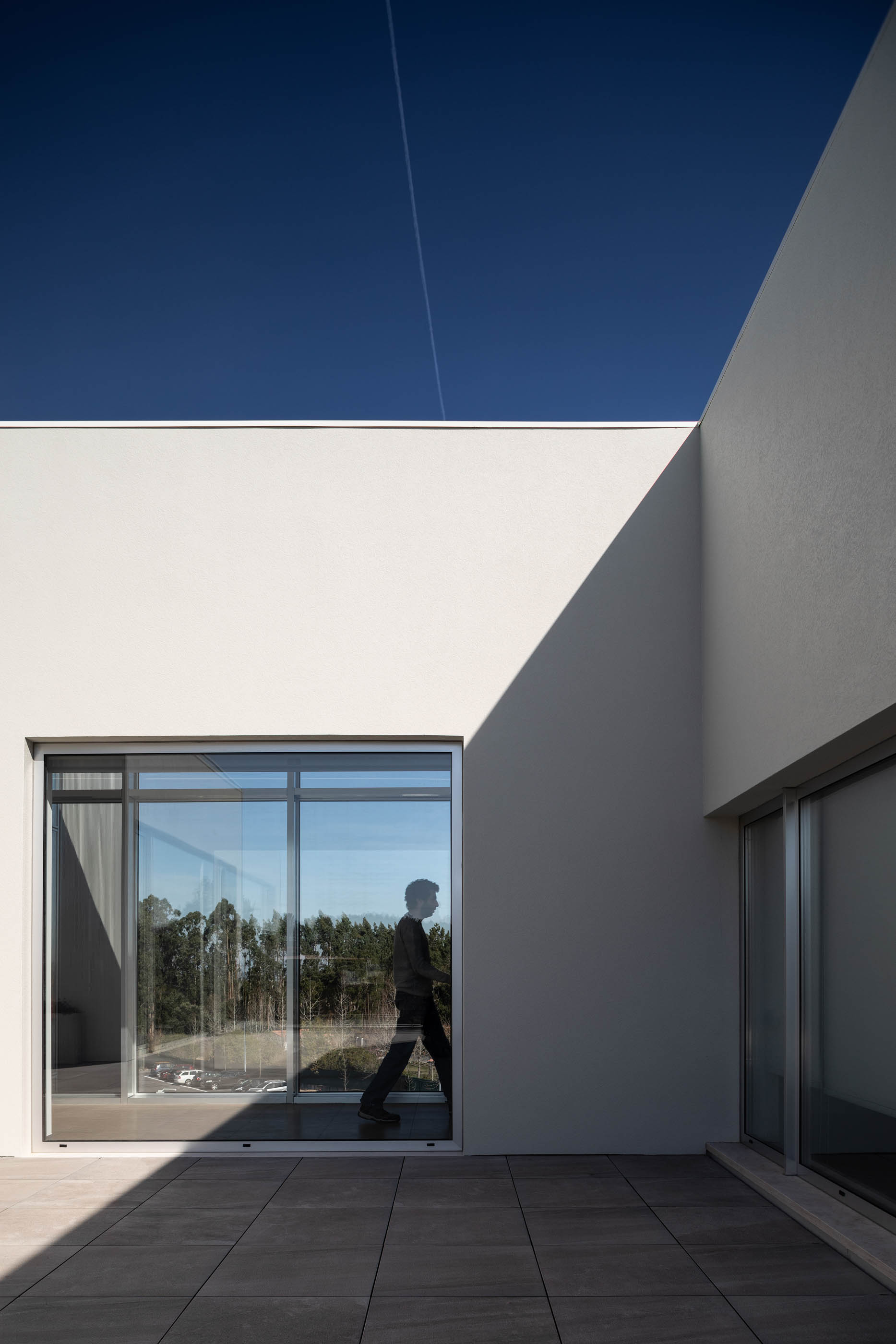 Pátio exterior com pavimento cerâmico, paredes brancas e amplas janelas envidraçadas. — Edifício Sede PRF arquitetura Impare Arquitectura em Portugal