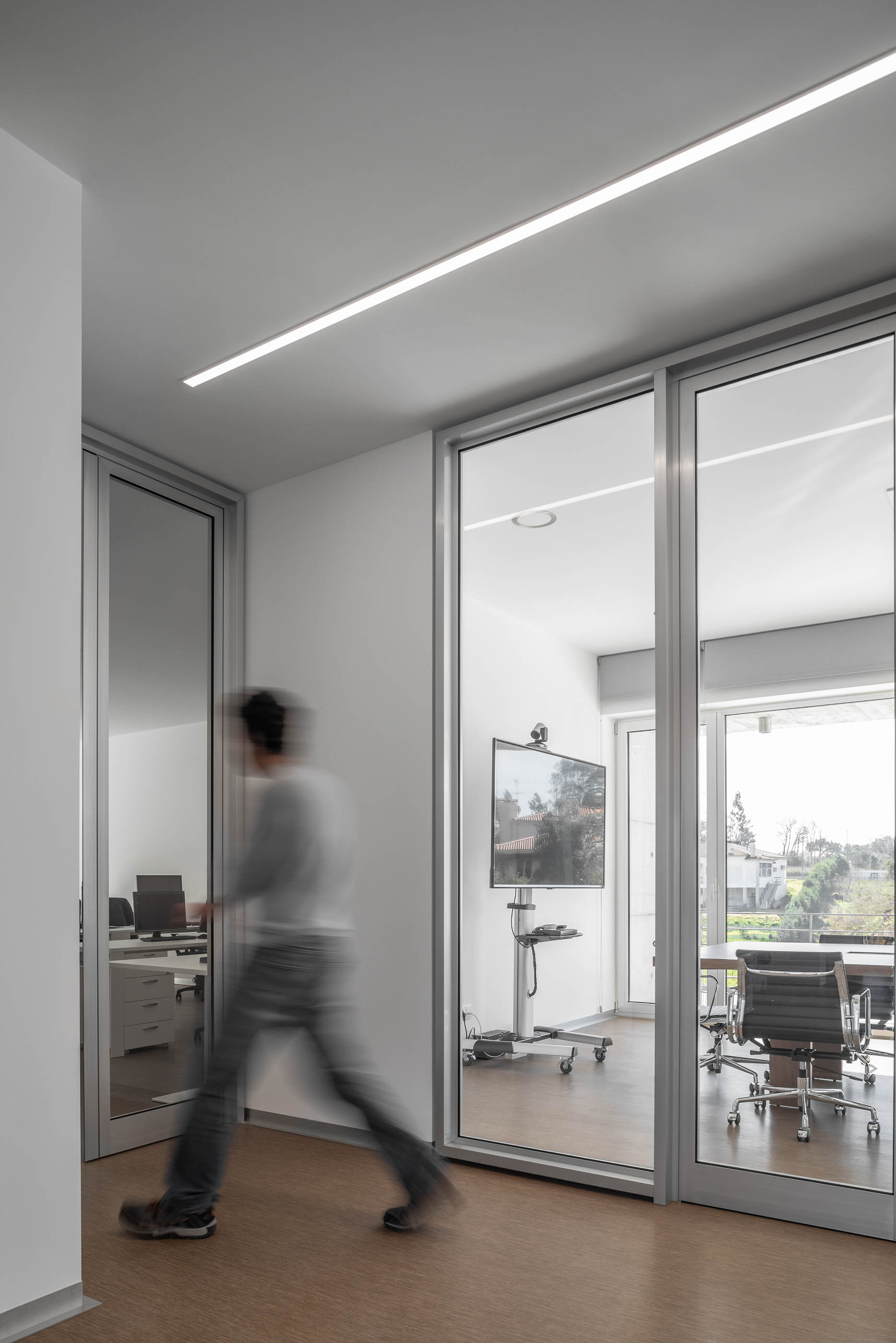 Espaço de circulação com divisórias de vidro, pavimento em cortiça e iluminação linear. — Edifício Sede PRF arquitetura Impare Arquitectura em Portugal