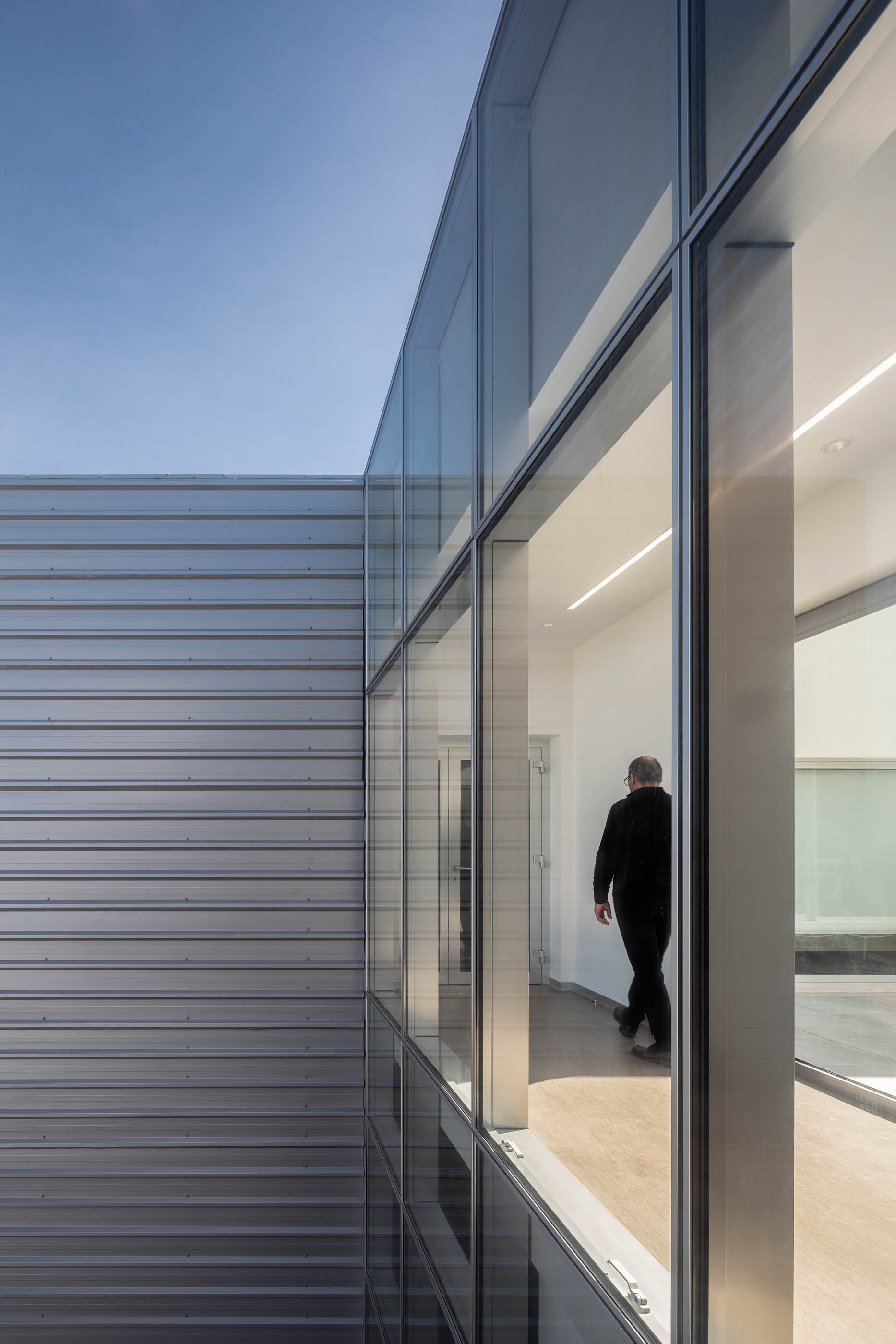Fachada com revestimento metálico e janelas amplas, corredor interior com pavimento em madeira. — Edifício Sede PRF arquitetura Impare Arquitectura em Portugal