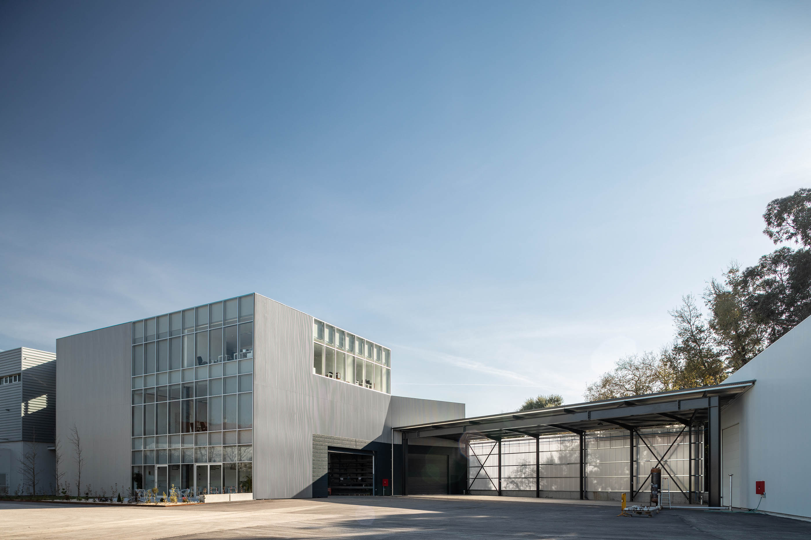 Vista exterior do edifício com revestimento metálico, estrutura metálica e zona de estacionamento. — Edifício Sede PRF arquitetura Impare Arquitectura em Portugal