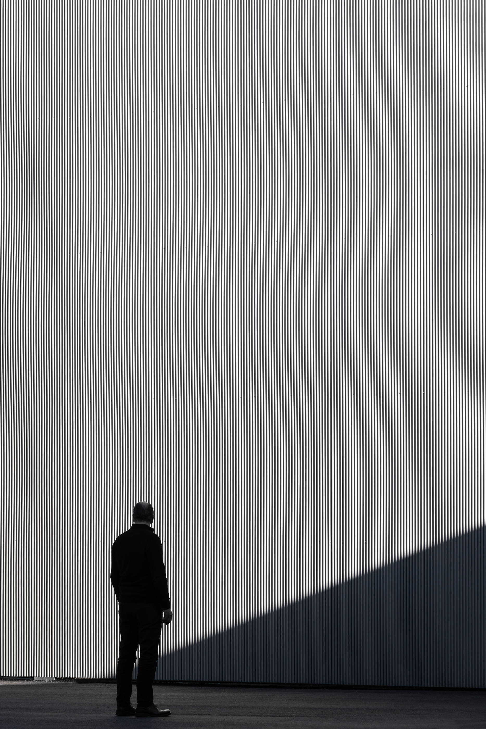 Homem em frente a fachada metálica canelada, em tons de cinza e preto, minimalista. — Edifício Sede PRF arquitetura Impare Arquitectura em Portugal