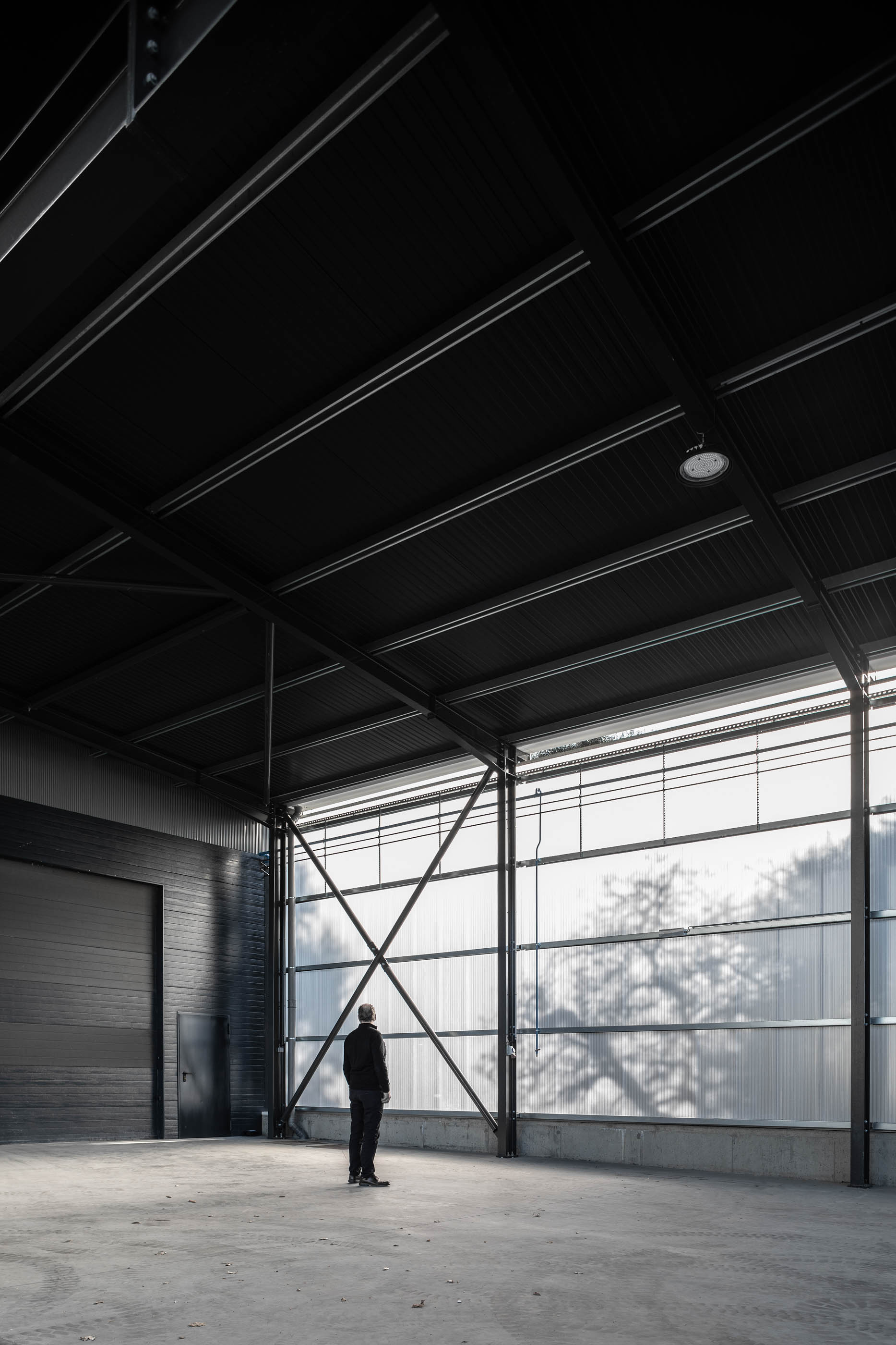 Interior de armazém com estrutura metálica aparente, paredes metálicas e luz natural filtrada. — Edifício Sede PRF arquitetura Impare Arquitectura em Portugal