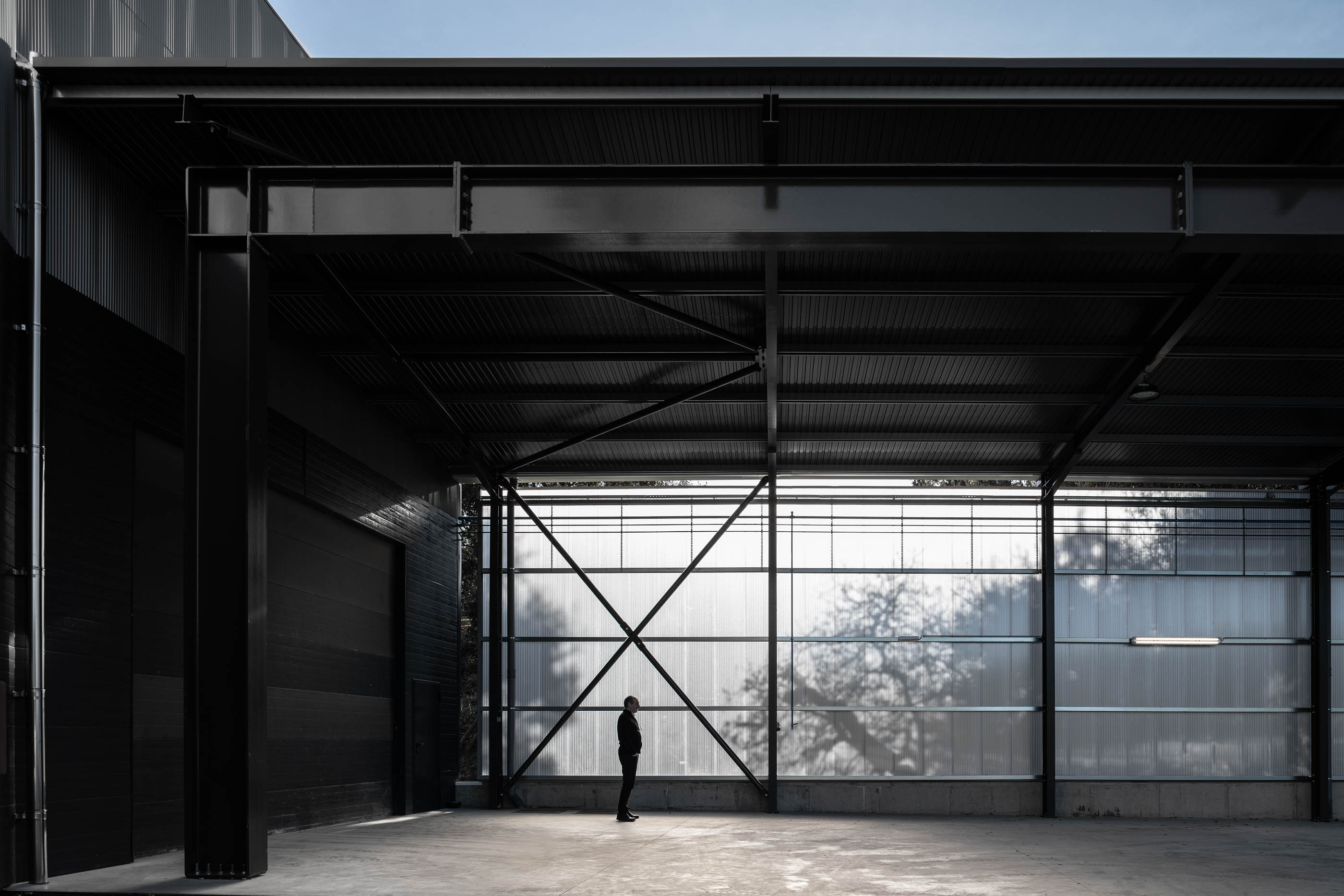 Estrutura metálica de armazém com paredes em chapa translúcida, piso em betão e iluminação. — Edifício Sede PRF arquitetura Impare Arquitectura em Portugal