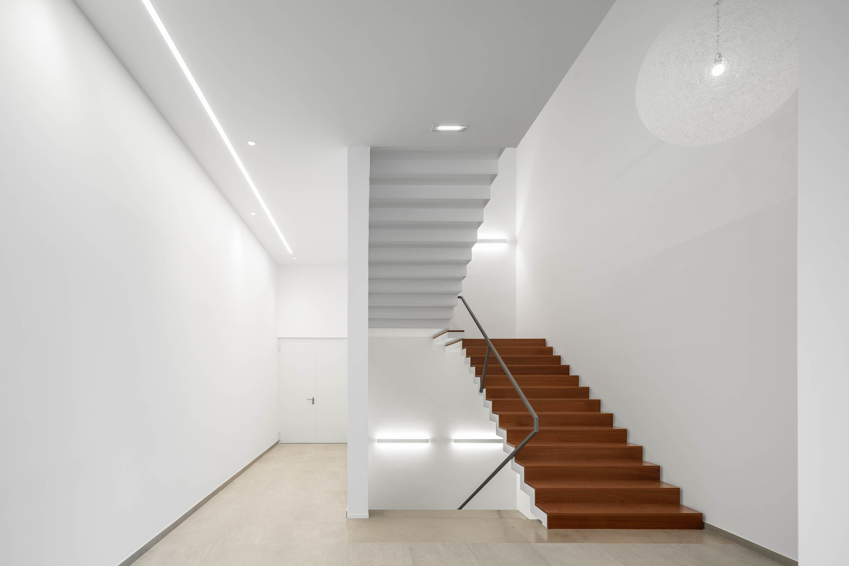 Hall de entrada com escadaria em madeira, balcão de receção e iluminação linear. — Edifício Sede PRF arquitetura Impare Arquitectura em Portugal