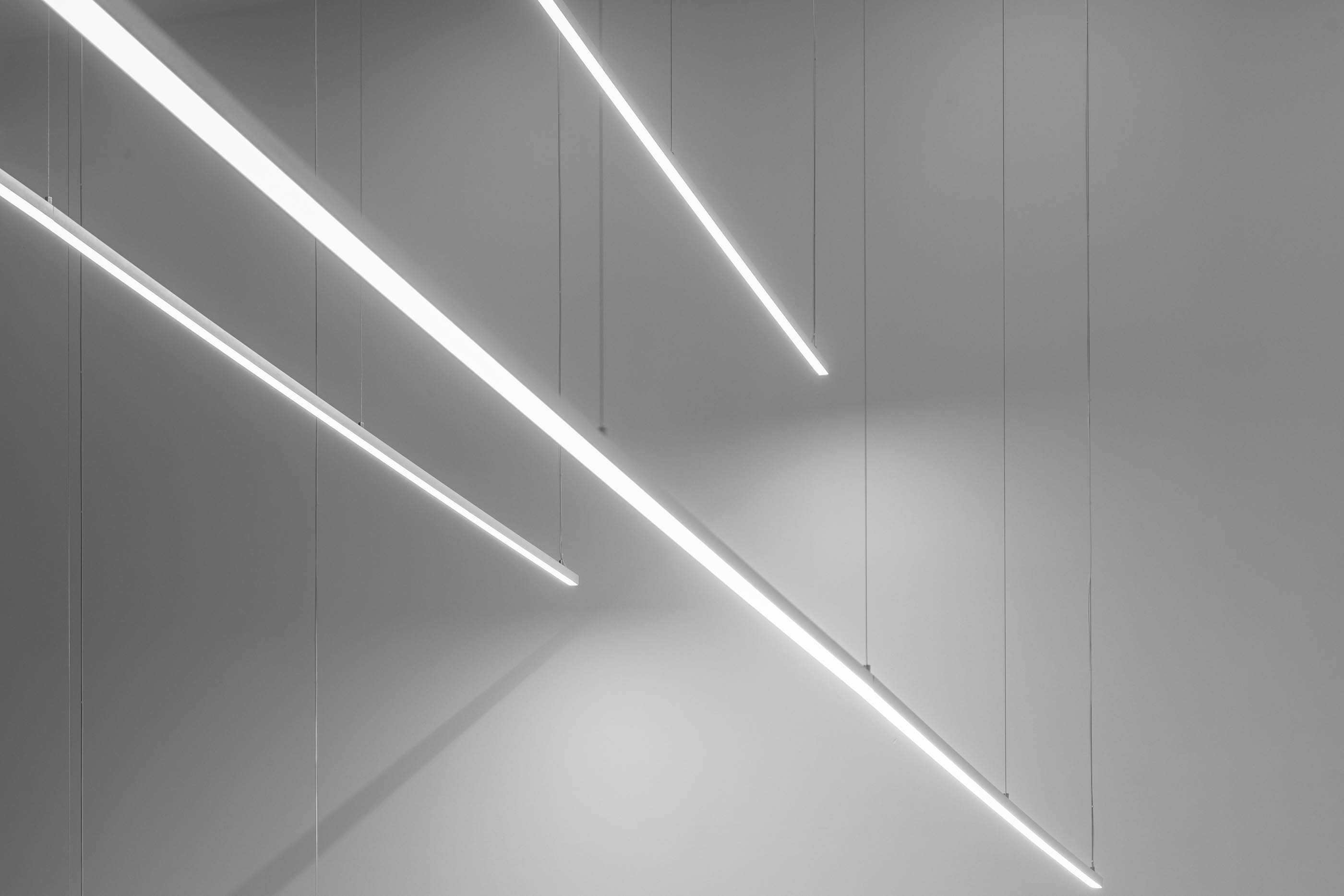 Iluminação suspensa com luminárias lineares, design moderno e minimalista em fundo cinza. — Edifício Sede PRF arquitetura Impare Arquitectura em Portugal