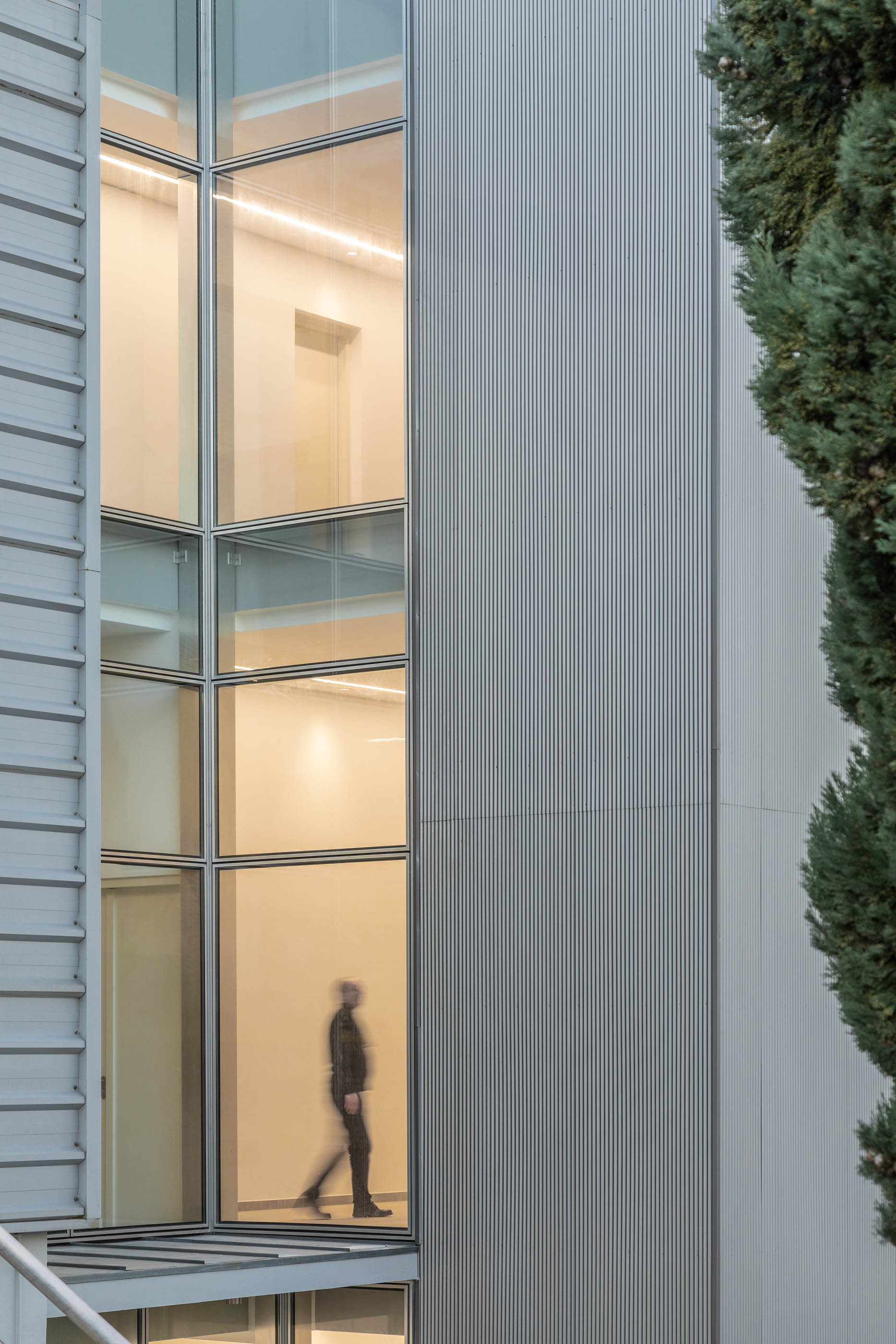 Fachada com revestimento metálico e janelas verticais, pessoa a caminhar no interior. — Edifício Sede PRF arquitetura Impare Arquitectura em Portugal
