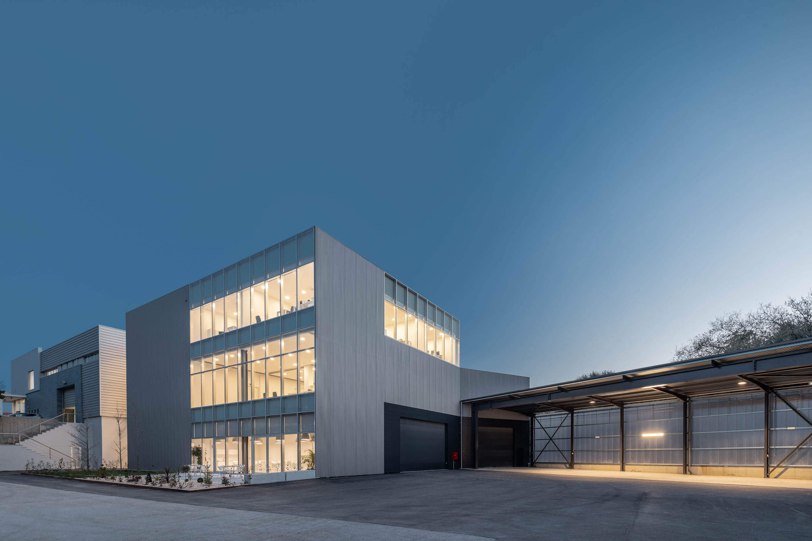 Vista noturna do edifício com iluminação interior, revestimento metálico e estrutura metálica. — Edifício Sede PRF arquitetura Impare Arquitectura em Portugal